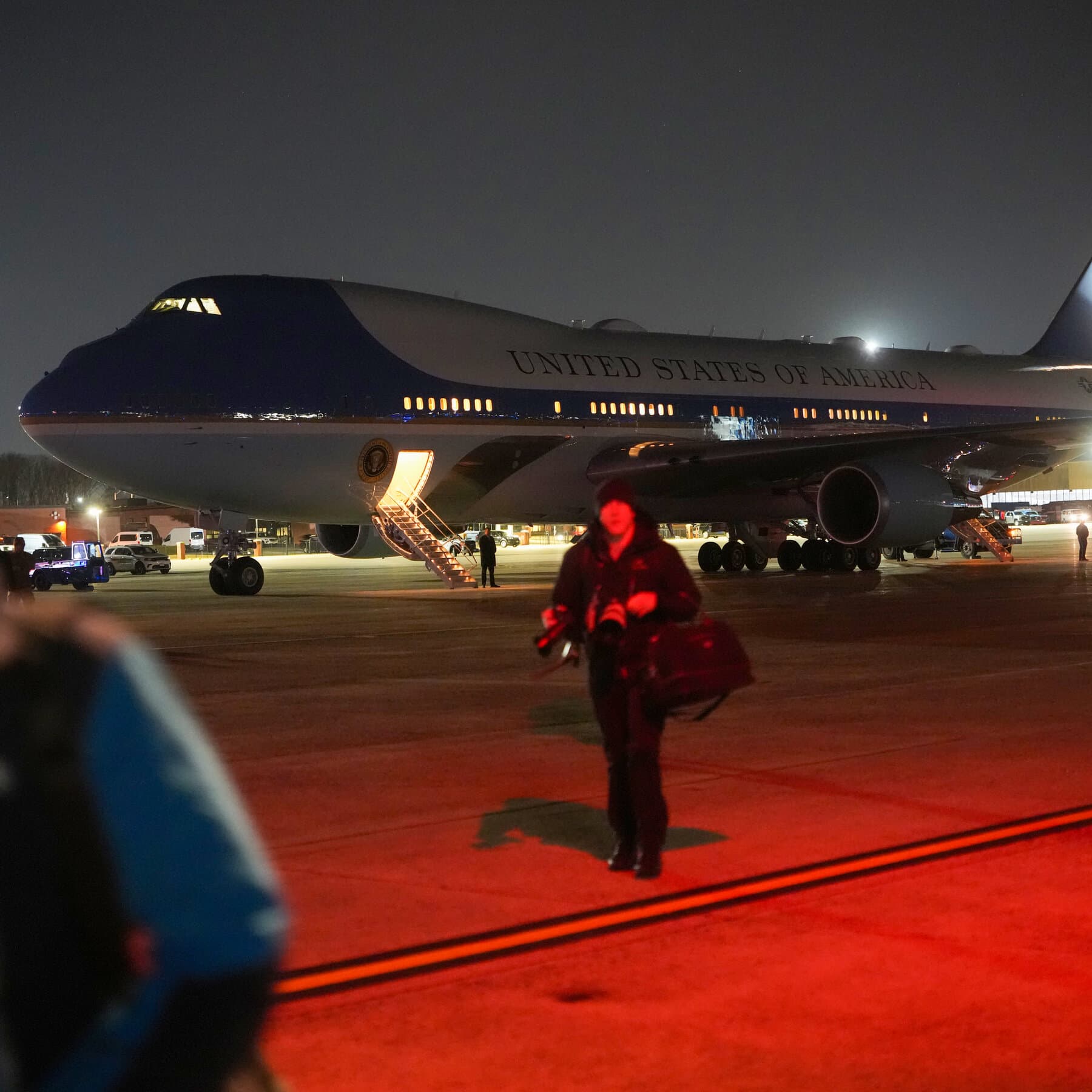 A gritty, cinematic wide shot of Air Force One mid-air, casting a long shadow over a gray, turbulent ocean. The plane is making an aggressive, tilting U-turn. One of the engines is emitting a faint, sickly green electrical spark. The sky is a heavy, cynical shade of charcoal, suggesting a storm of bureaucracy and decay. Digital art style, highly detailed, somber atmosphere.