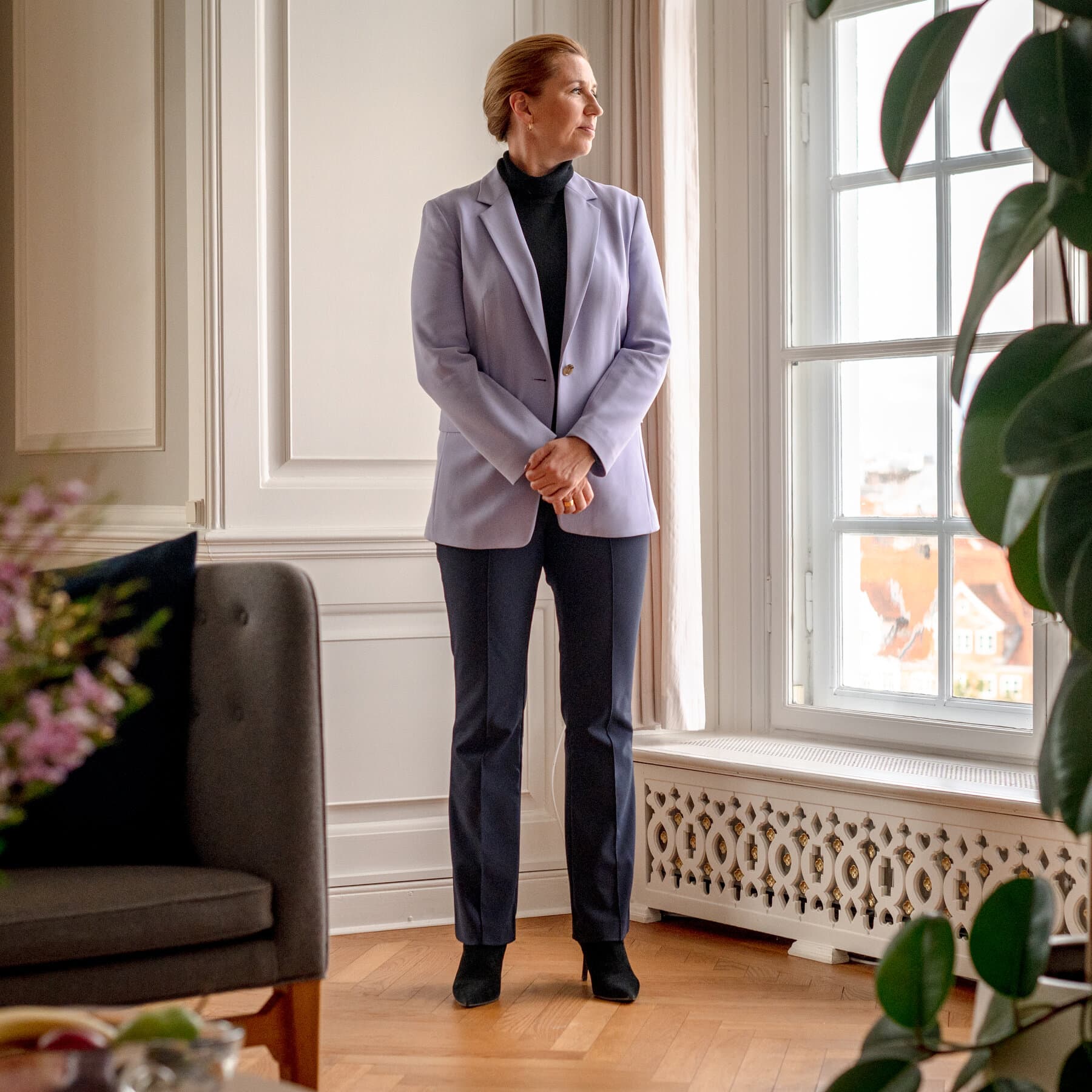 A satirical political cartoon style illustration showing a small, stern Danish woman in a business suit standing firmly in front of a giant map of Greenland. She is holding up a hand in a 'stop' gesture. On the other side, a large, shadowy figure with a long red tie and bad hair is holding a giant bag of money and a 'Sold' sign. The background is icy blue with subtle cracks in the ice. The style should be caricature, exaggerated features, high contrast.