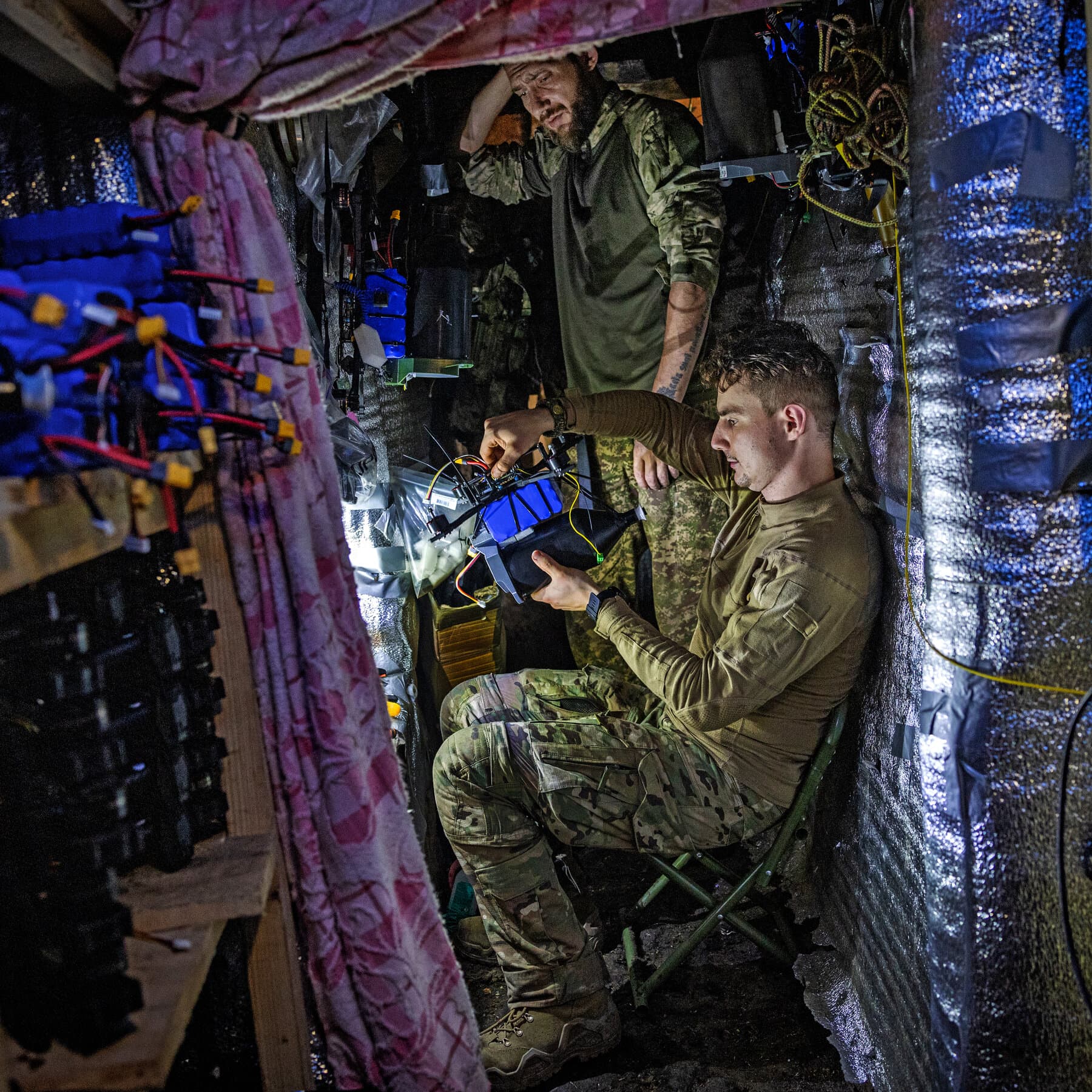 A hyper-realistic, cynical illustration contrasting a massive, rusted tank stuck deep in thick, frozen mud with a swarm of small, sleek drones buzzing effortlessly overhead against a grey, snowy winter sky. The scene should feel cold and desolate. In the foreground, a single pristine snowflake lands on a dirty remote control.