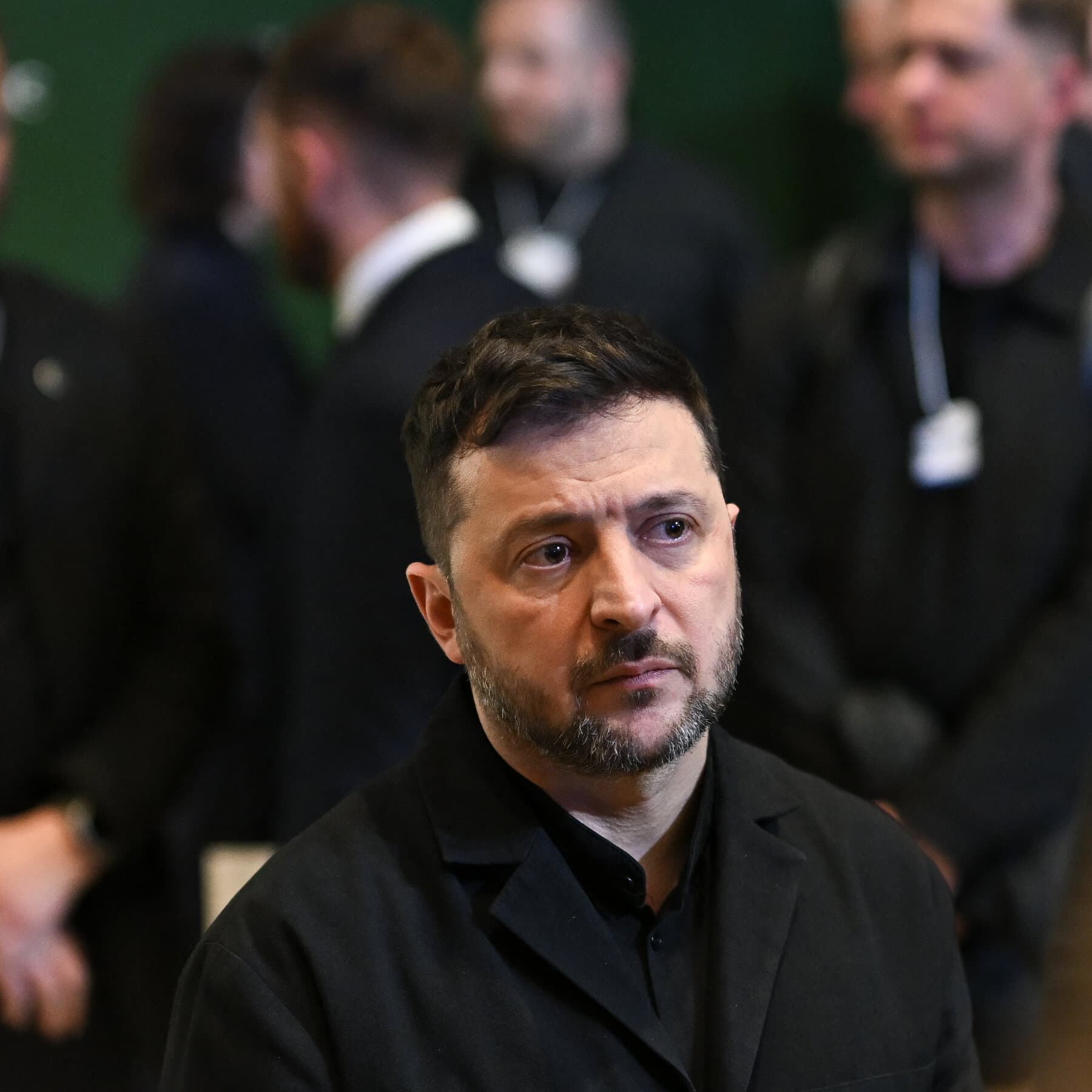 A satirical, hyper-realistic oil painting of a peace negotiation table set in the middle of a vast, hot desert. Three empty business suits are sitting in the chairs—one with an American flag pin, one with a Russian flag pin, and one with a Ukrainian flag pin—but there are no people inside the suits. On the table, there is a silver platter with a single, tiny sandwich. In the background, a mirage of a snowy, ruined city flickers in the heat waves. The sky is an oppressive, bright blue.
