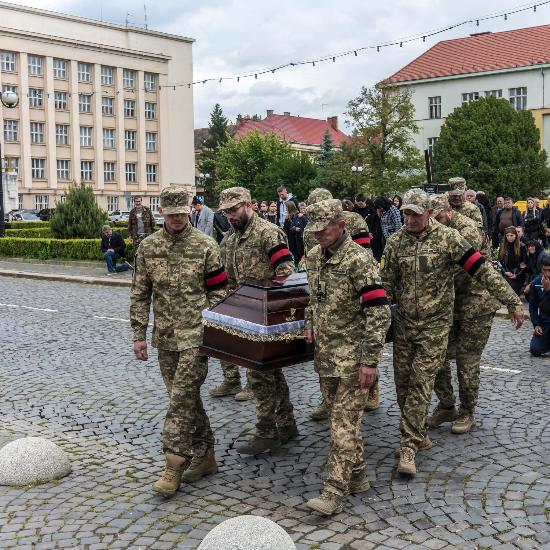 A gritty, cynical illustration in a comic book noir style. A large, rusty, mechanical meat grinder sits on a table. The handle is being turned by a generic business suit with no face. The output of the grinder is a pile of medals and coins. In the background, a dark, muddy field with gray smoke. High contrast, dark moody colors.