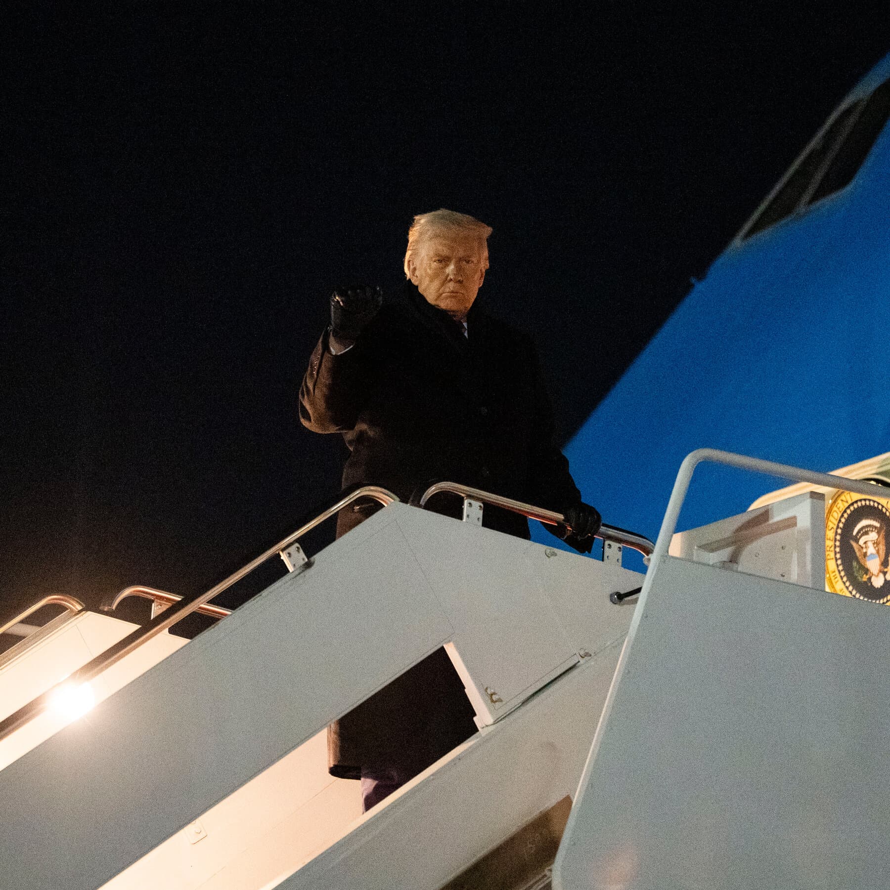 A satirical, gritty political cartoon style image. A large, oversized orange hand reaches across the Atlantic Ocean from the left, trying to grab a massive, icy chunk of land labeled 'Greenland'. On the right side, representing Europe, tiny angry men in suits are shaking their fists and looking panicked. High contrast, dark humor atmosphere.