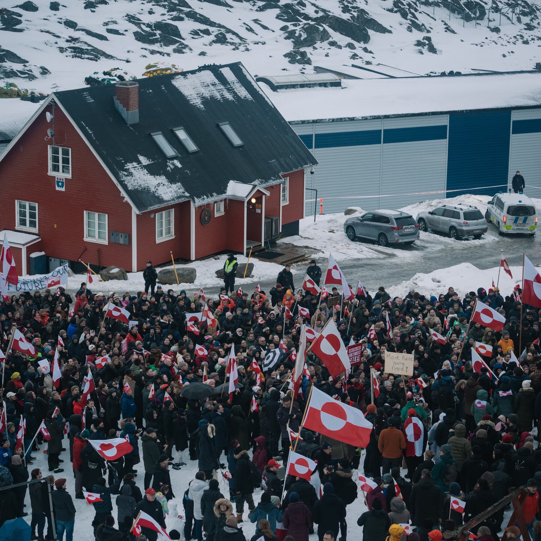 A gritty, conceptual editorial illustration showing a map of Greenland leaning away in horror from a burning, chaotic map of the United States, while seeking shelter behind a calm, sturdy Danish flag. High contrast, cynical tone.