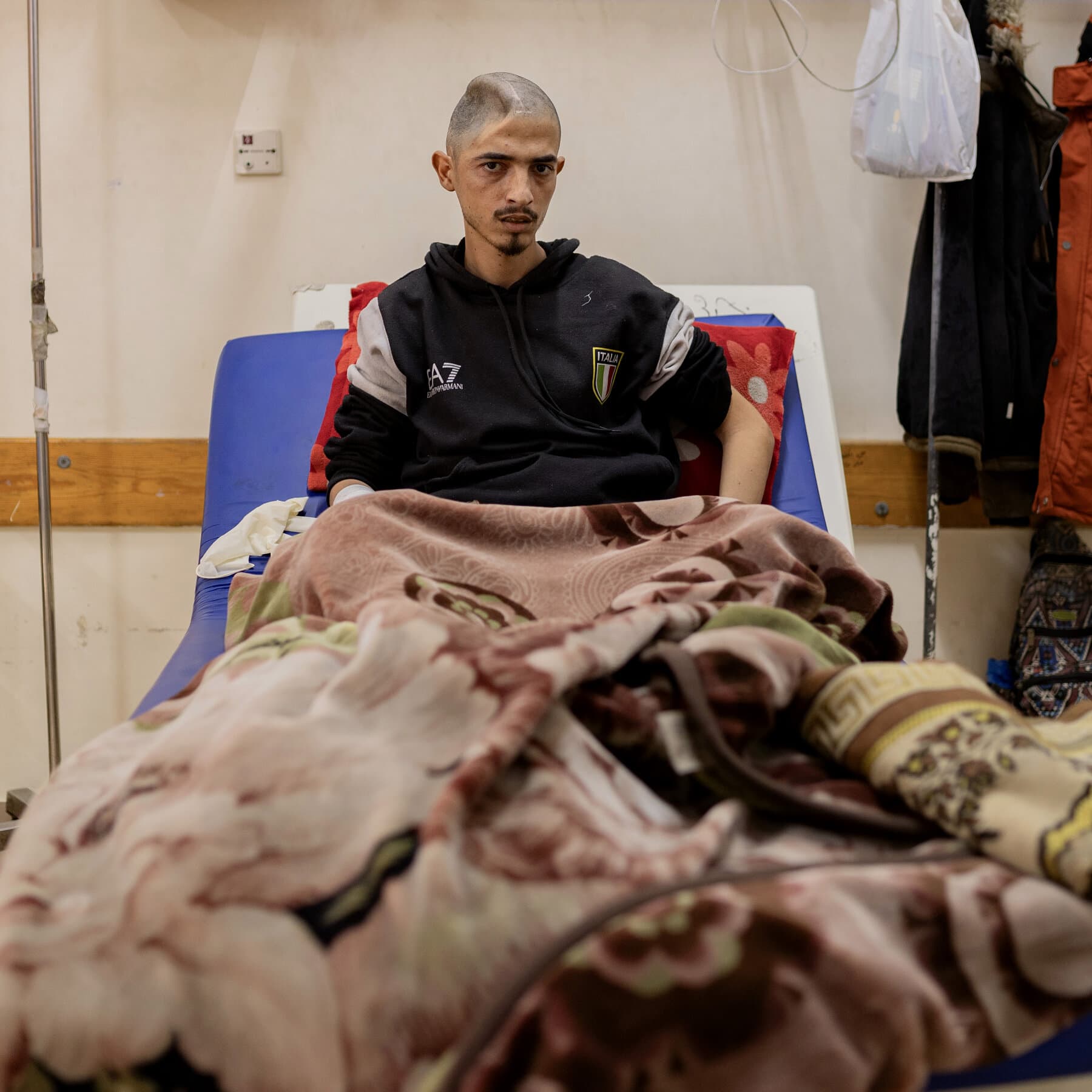 A stark, high-contrast black and white illustration of a heavy, rusted iron gate standing alone in a vast, empty desert. The gate is slightly ajar, just a crack, letting through a single beam of blinding white light that cuts through the dusty, dark atmosphere. In the foreground, shadowy, indistinct figures are huddled together, waiting. The style should be gritty and textured, emphasizing isolation and the oppressive weight of the barrier.