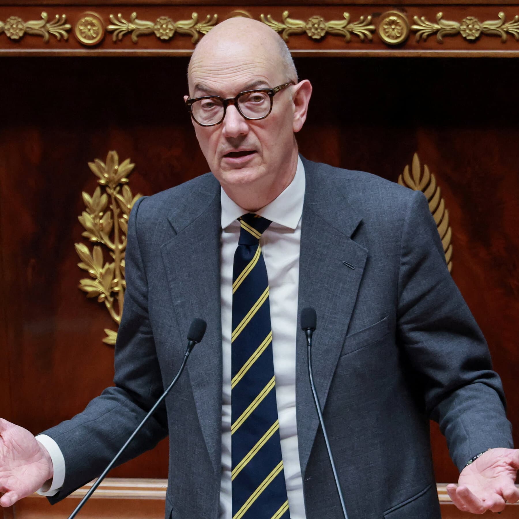 A high-contrast, gritty comic book style illustration. In the center, a pair of expensive suit sleeves shaking hands with a tactical police glove. The handshake is dripping with thick black ink that pools on the floor. In the background, a blurred, grey crowd of people are shouting, but they have no mouths. The lighting is harsh and creates deep shadows. The color palette is strictly black, white, and dark green.