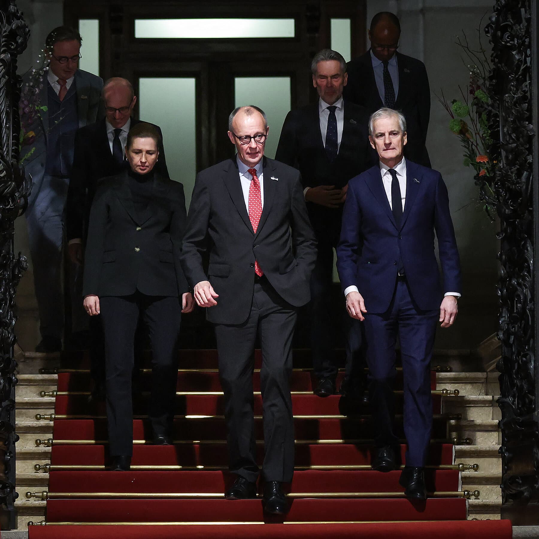 A dimly lit, luxurious dining room in a European palace where worried politicians in suits are huddled around a long table filled with half-eaten gourmet food and wine, looking anxious. In the background, a large map of Greenland hangs on the wall, slightly crooked. The atmosphere is tense and cynical.