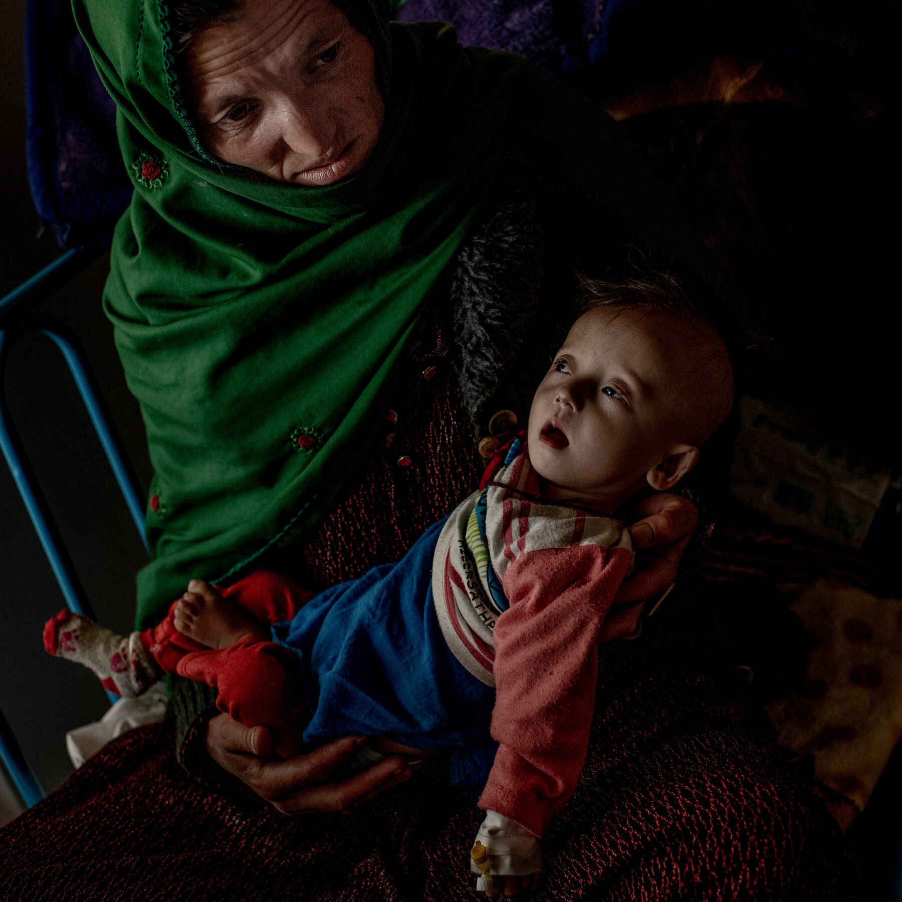 A desolate, dusty landscape in rural Afghanistan, an abandoned concrete clinic with a rusted padlock on the door, wind blowing dust, gray and brown tones, stark and depressing atmosphere, no people visible, high contrast.