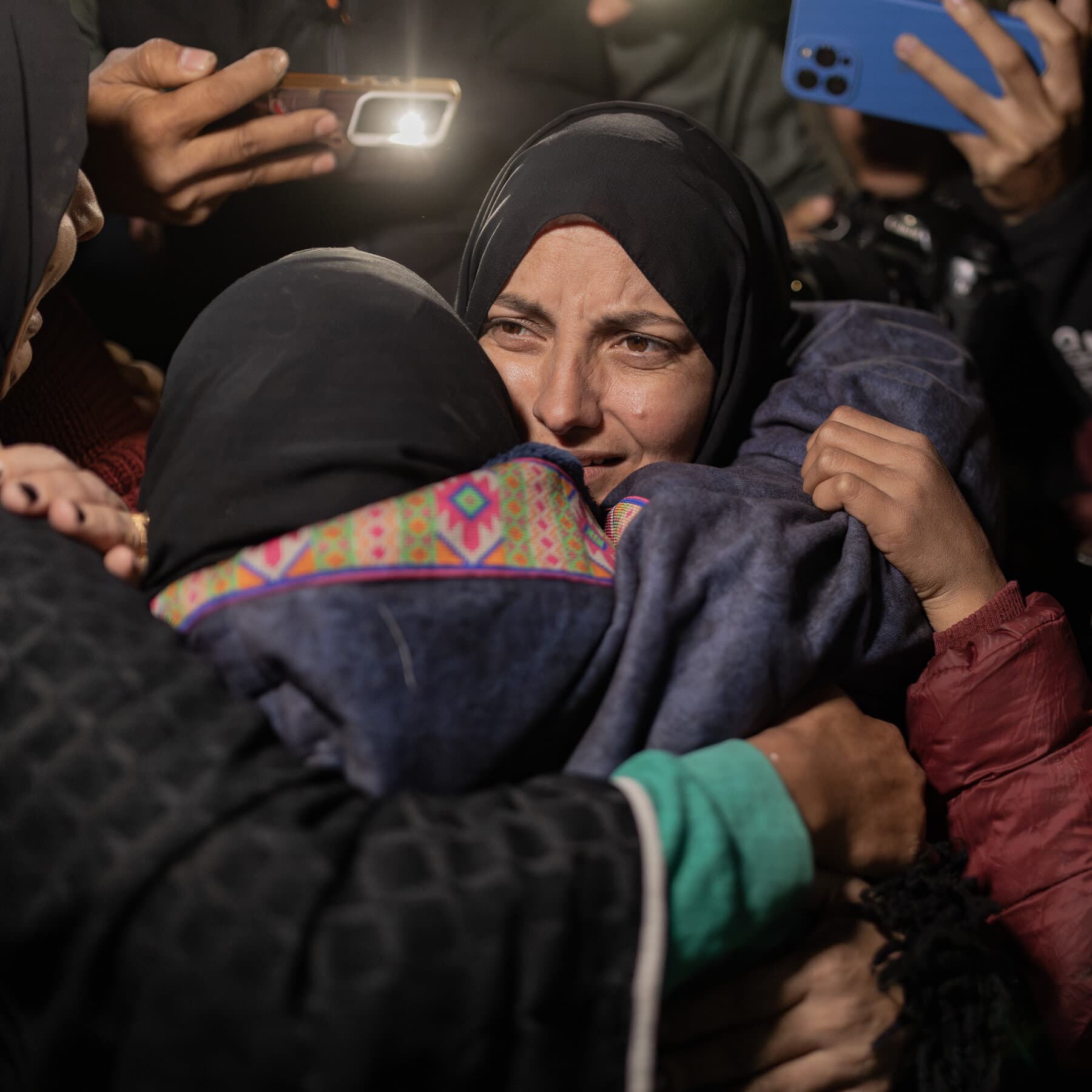 A rusty, heavy iron gate in a dusty desert border wall, slightly ajar, with a vast empty space in front of it and a very small group of silhouetted people walking through, stark lighting, cynical atmosphere.
