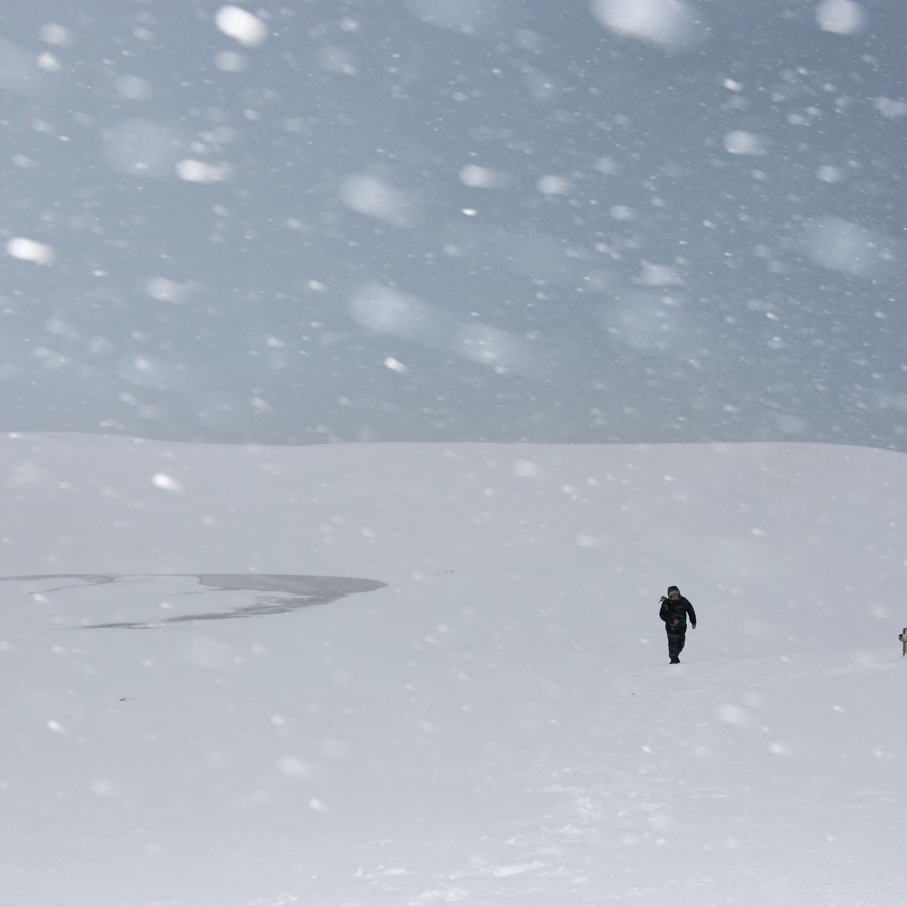 A desolate street in a Japanese town buried under massive 6-foot walls of white snow. The sky is grey and heavy. A single, small figure is struggling to shovel a path. Power lines are sagging under the weight of ice. The atmosphere is cold, gloomy, and hopeless. High contrast, realistic style.