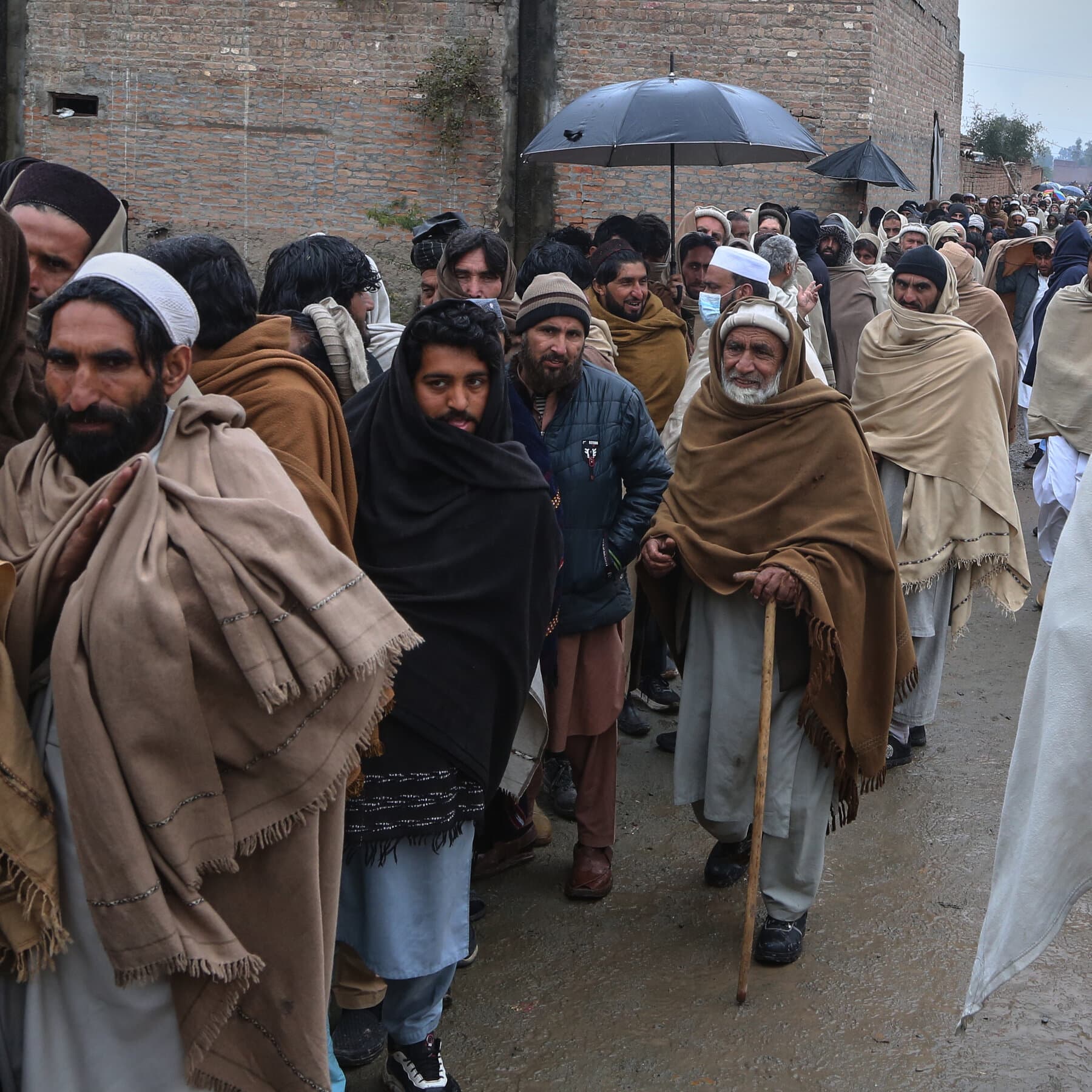 A desolate, dusty landscape in Pakistan with a long line of displaced civilians carrying bundles, hazy atmosphere, muted earth tones, realistic photojournalism style.