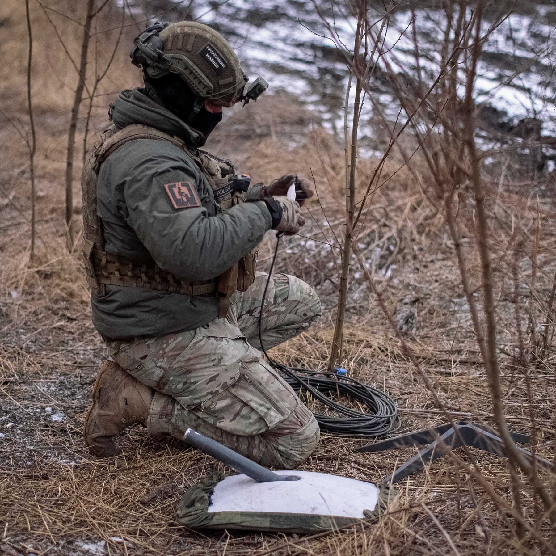 A gritty, muddy trench scene where a soldier in generic military gear looks frustratedly at a portable satellite dish that is dark and inactive, while holding a rugged tablet displaying a 'No Connection' error icon, grey overcast sky, realistic style.