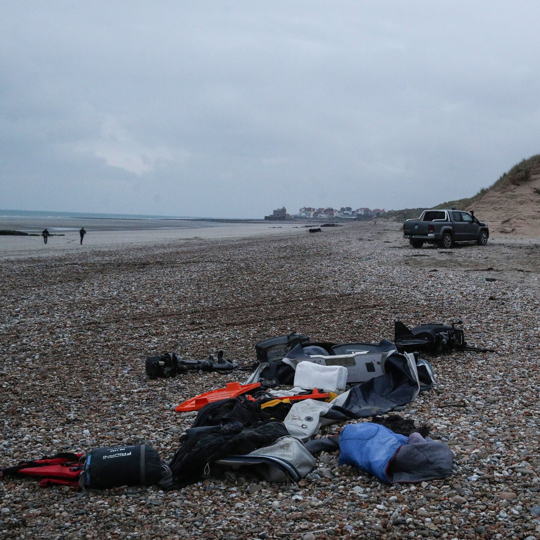 A dark, moody abstract image of a vast, rough dark blue ocean at night. In the distance, vague lights of a city on the horizon are blurred by fog. In the foreground, empty dark waves crash. The feeling is cold, isolated, and hopeless. No people, just the overwhelming emptiness of the sea.