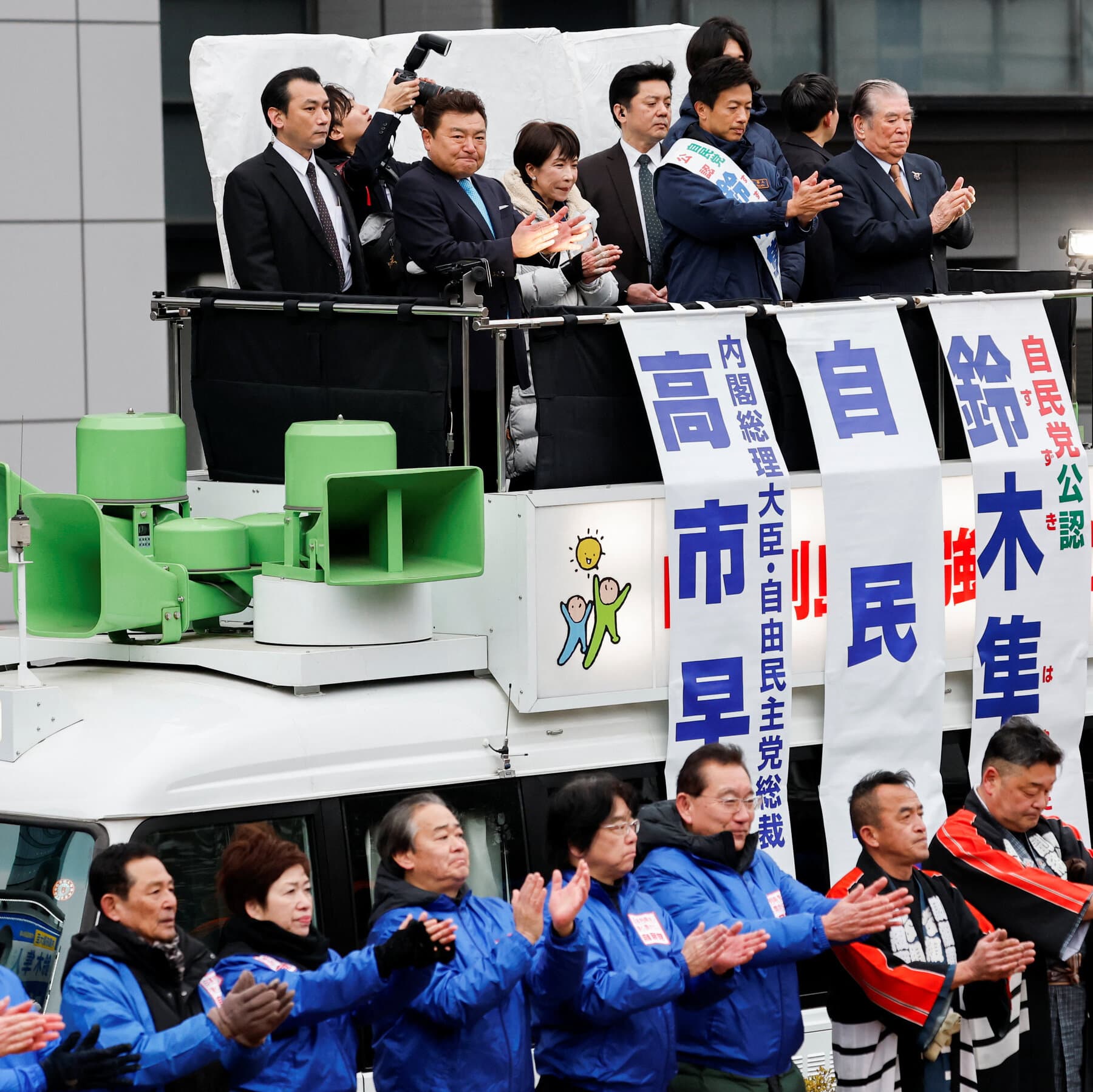 A highly cynical editorial illustration in a gritty style. A generic, faceless female politician standing on a podium made of old, gray concrete blocks. She is wearing a bright, colorful sash that contrasts with the dull surroundings. Below the podium, a sea of identical, faceless people in suits are clapping robotically. The sky is a heavy, smoggy gray. No text.