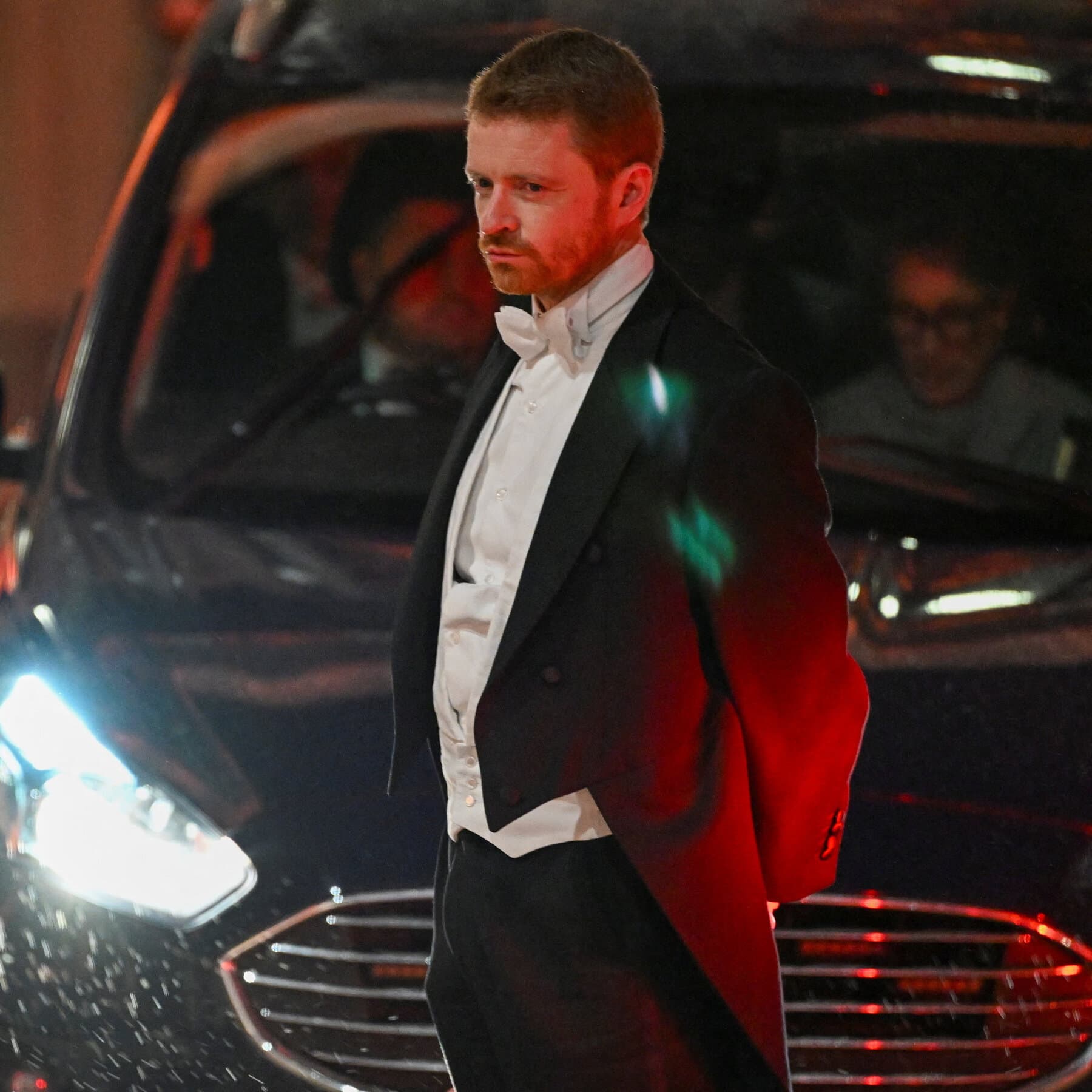 A hyper-realistic, gloomy image of a generic government office desk in London. The desk is cluttered with papers, a tipped-over cup of tea spilling onto a resignation letter. In the background, out of focus, a television screen shows a news broadcast with a blurred image of a politician. The lighting is cold and grey, emphasizing a mood of failure and bureaucratic collapse.
