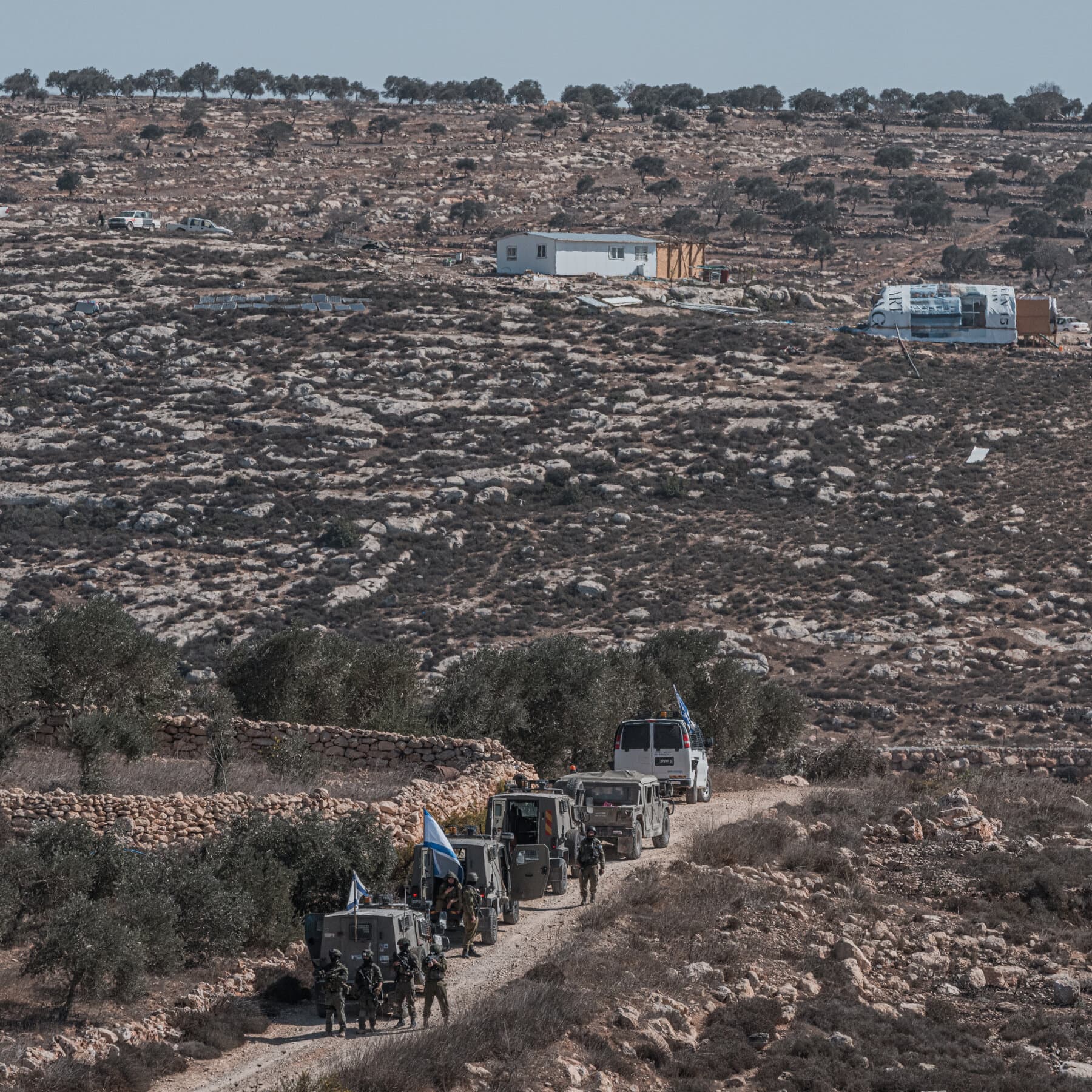 A gritty, high-contrast illustration of a stack of legal documents and maps sitting on a dusty, rocky ground, with a construction crane silhouette in the distance against a harsh sun. No text.