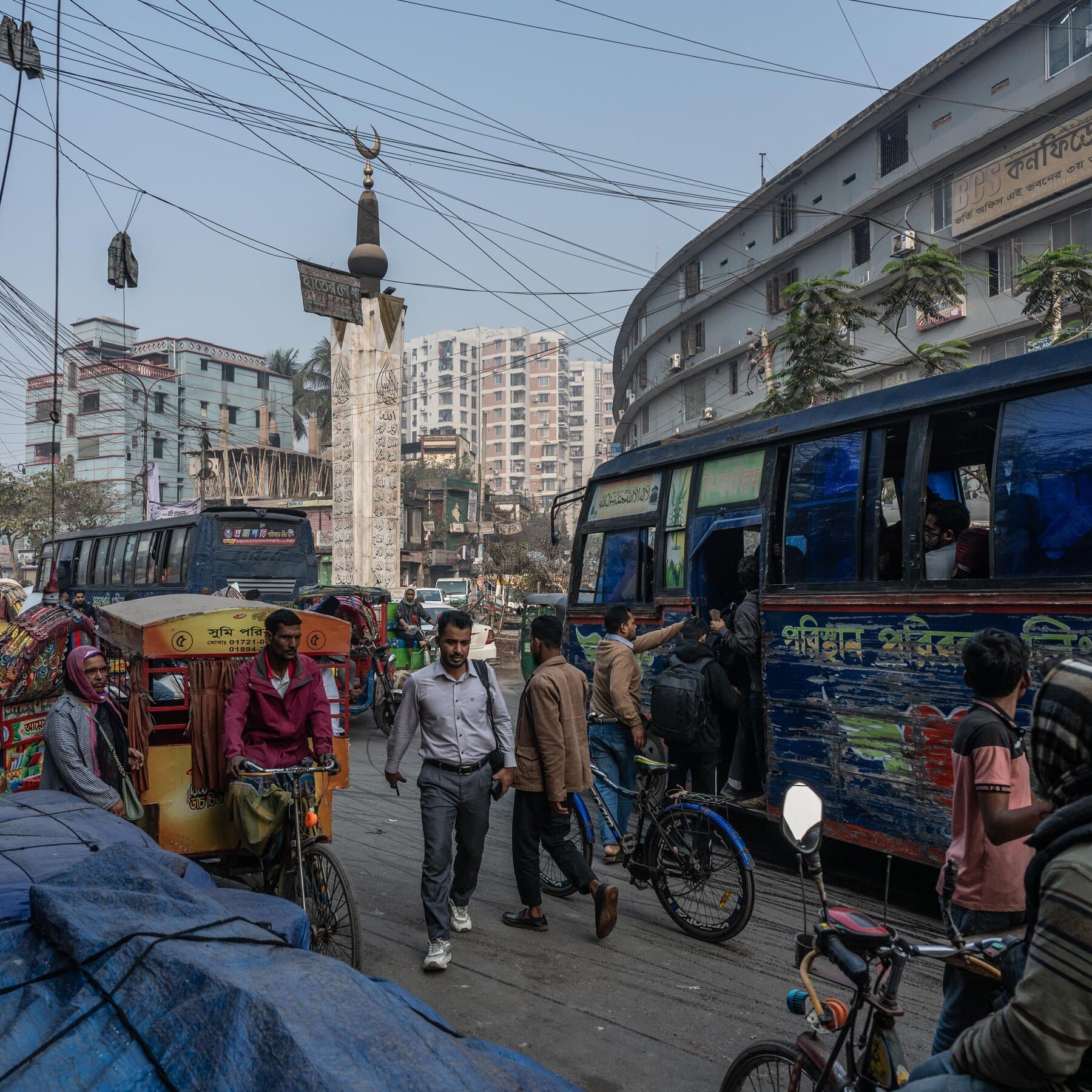 A gritty, slightly desaturated street scene in Bangladesh showing a worn-out ballot box sitting on a dusty table. In the background, a faded, torn poster from a student protest is peeling off a brick wall. The lighting is overcast and gloomy, capturing a mood of exhaustion and cynicism rather than celebration. No text.