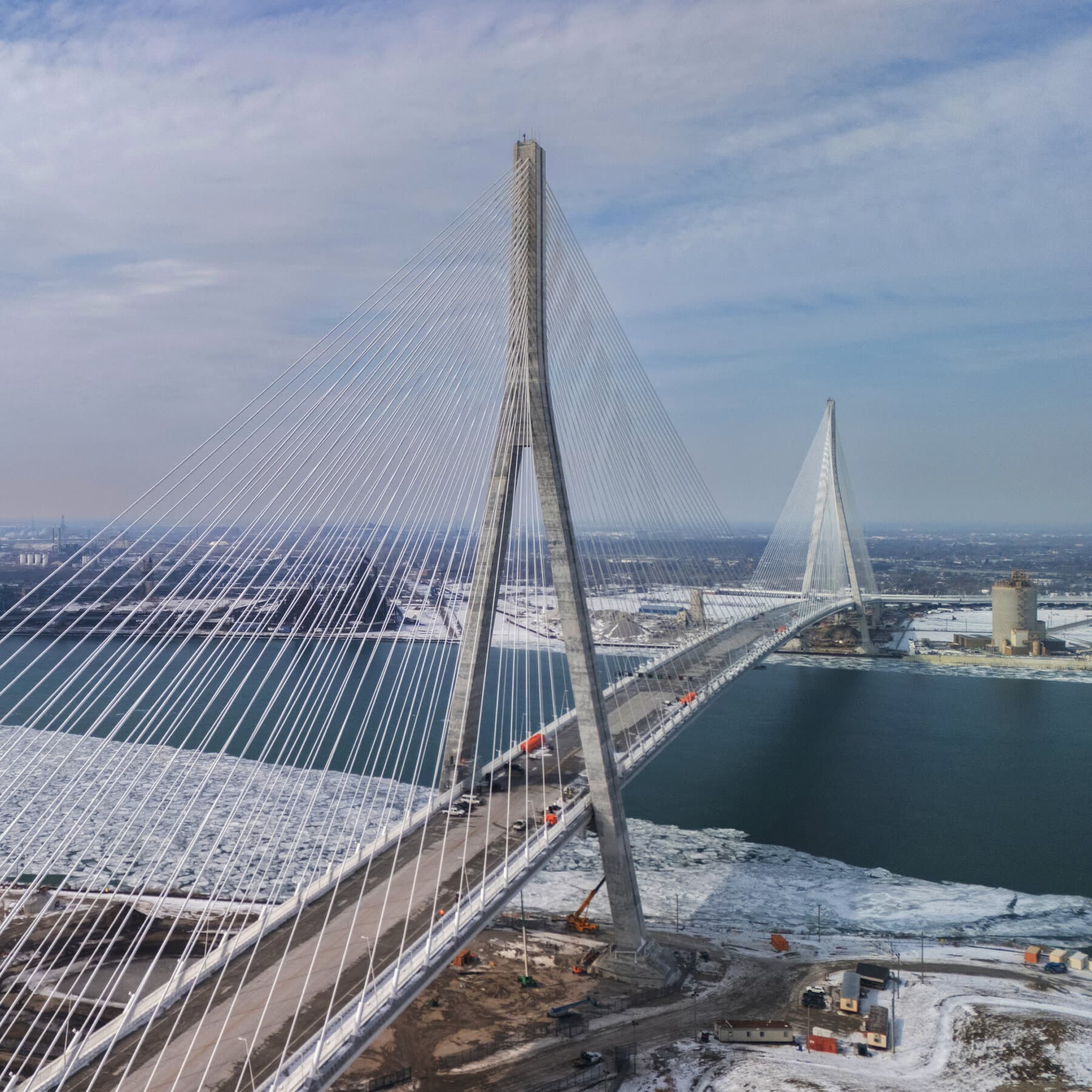 A gritty, satirical illustration in a noir comic style. In the foreground, a shadowy figure in a suit hands a golden key to another man in a suit across a fancy dining table. In the background, visible through a window, a massive modern suspension bridge is blocked by red 'DO NOT ENTER' tape and a comical, oversized padlock. The sky is gloomy and grey.
