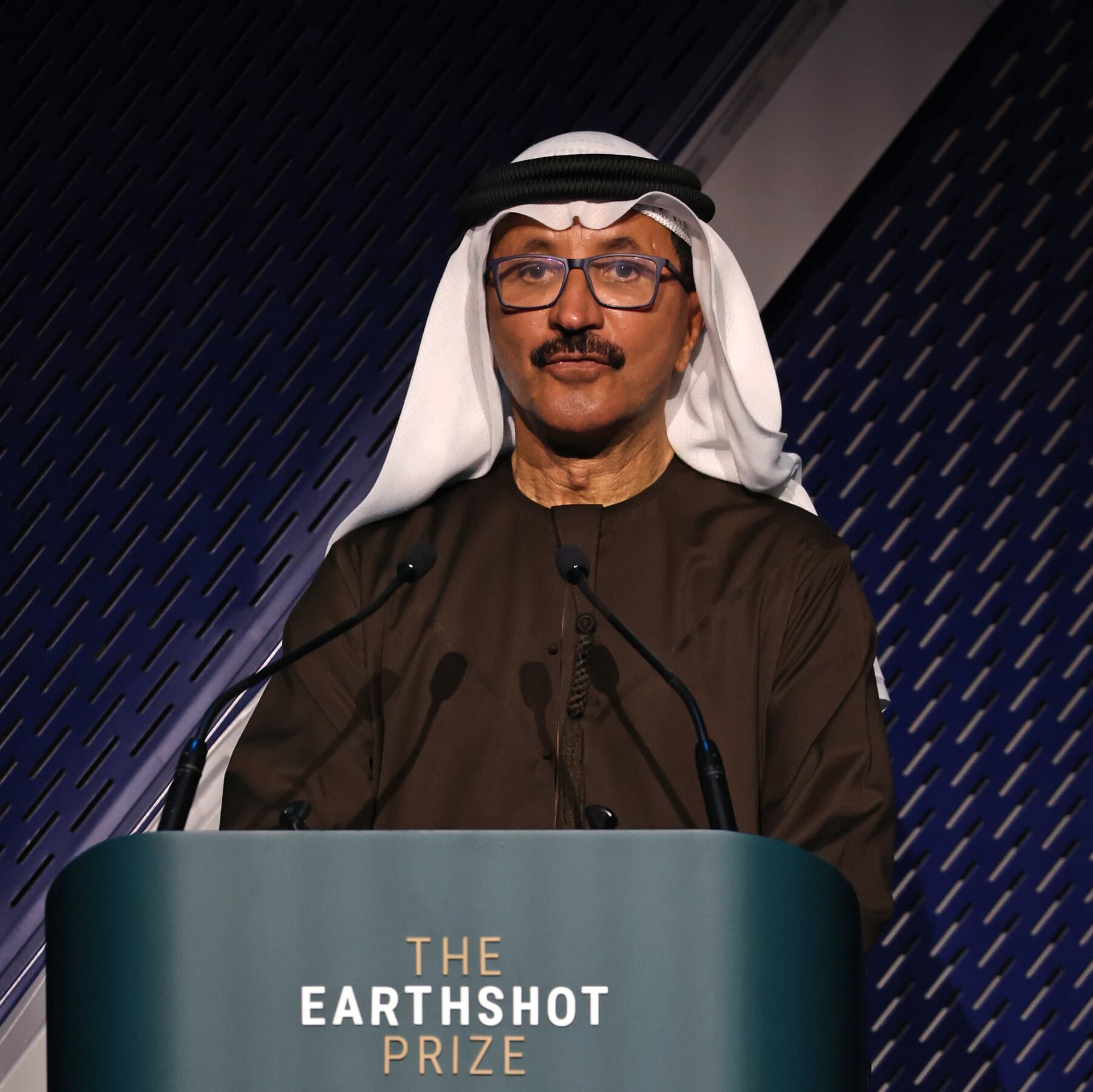 A single, empty, high-end executive office chair sitting alone on a shipping dock at sunset. In the background, massive container ships and towering cranes loom over the small chair. The lighting is moody and dramatic, symbolizing a fall from power amidst a giant industry.