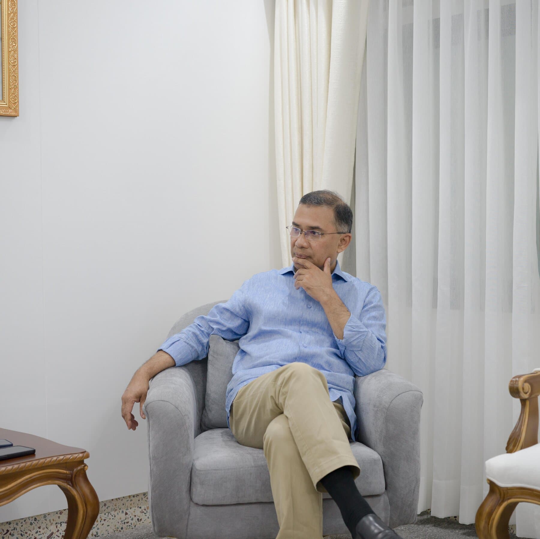 A worn-out theater stage with a dusty red velvet curtain. On the stage, a single spotlight shines on an empty, ornate wooden throne. The floor of the stage is littered with old, trampled confetti and discarded campaign flyers. The atmosphere is dim, moody, and slightly decaying, capturing a sense of faded glory and repetitive history.