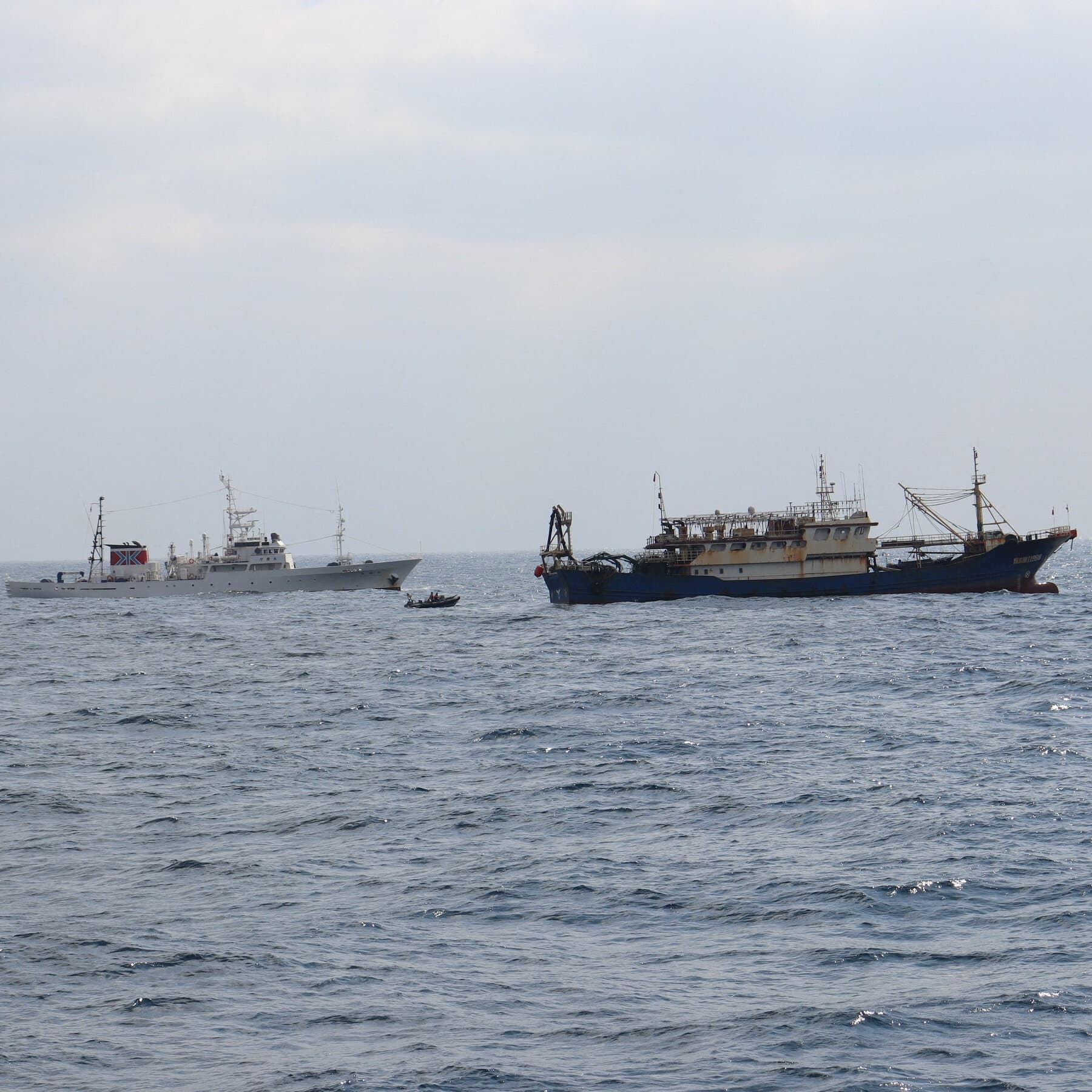 A gritty, gray-scale illustration of a fishing trawler alone in a vast, dark ocean, with ominous, exaggerated red border lines drawn on the surface of the water trapping it, viewed from high above, cynical art style.