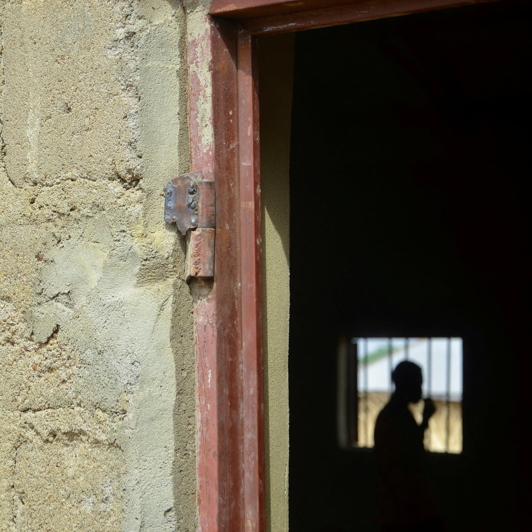 A gritty, photo-journalistic image of modern US military boots stepping onto dusty red African soil, contrasting with the sandals of a local bystander. The background is slightly blurred, showing the silhouette of a heavy transport plane and the heat haze of a sweltering afternoon.