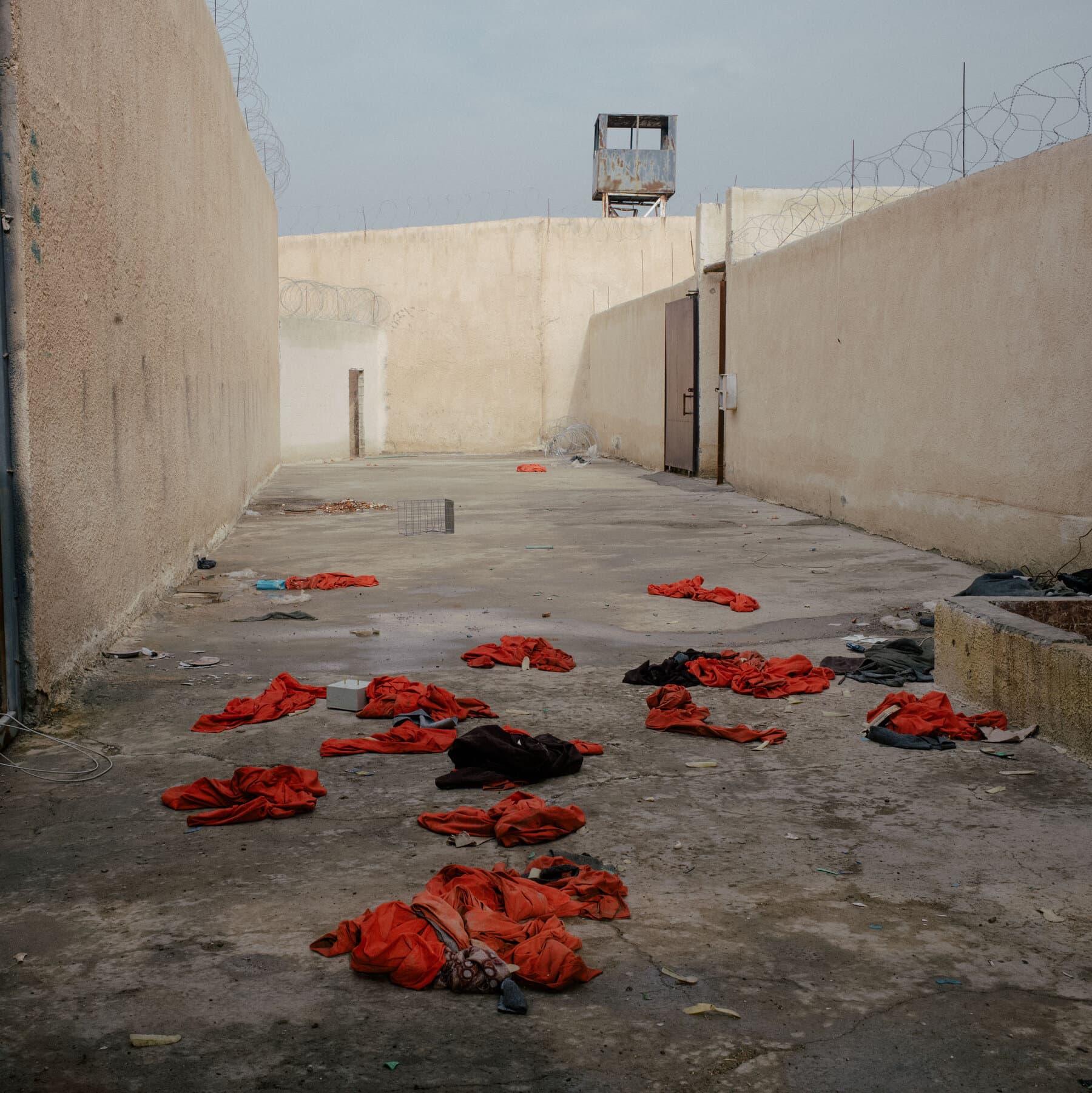 A conceptual illustration of a rusting, open padlock hanging on a chain-link fence in a desolate desert landscape. In the background, blurred silhouettes of people are walking away into a dust storm. The lighting is harsh and amber-colored, evoking a sense of abandonment and decay. The style should be gritty and realistic with a cynical, noir atmosphere.