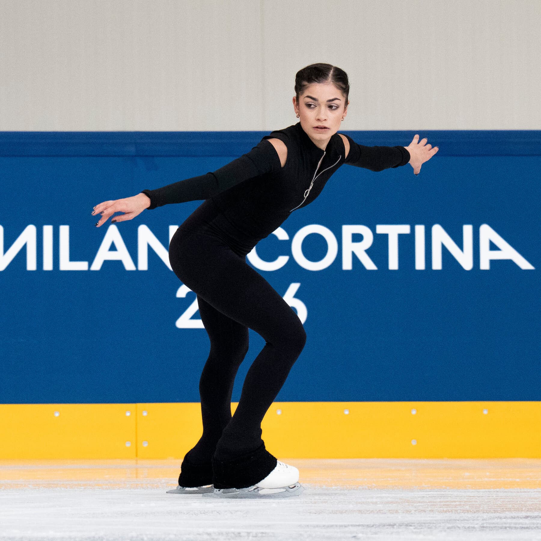 A hyper-realistic, moody, cinematic shot of a solitary female figure skater standing on a large ice rink. She is small in the frame, surrounded by the vast, empty white ice. The background is a dark arena with only a few harsh spotlights cutting through the gloom, creating long, dramatic shadows that stretch out from her skates. The atmosphere is cold, lonely, and ominous.