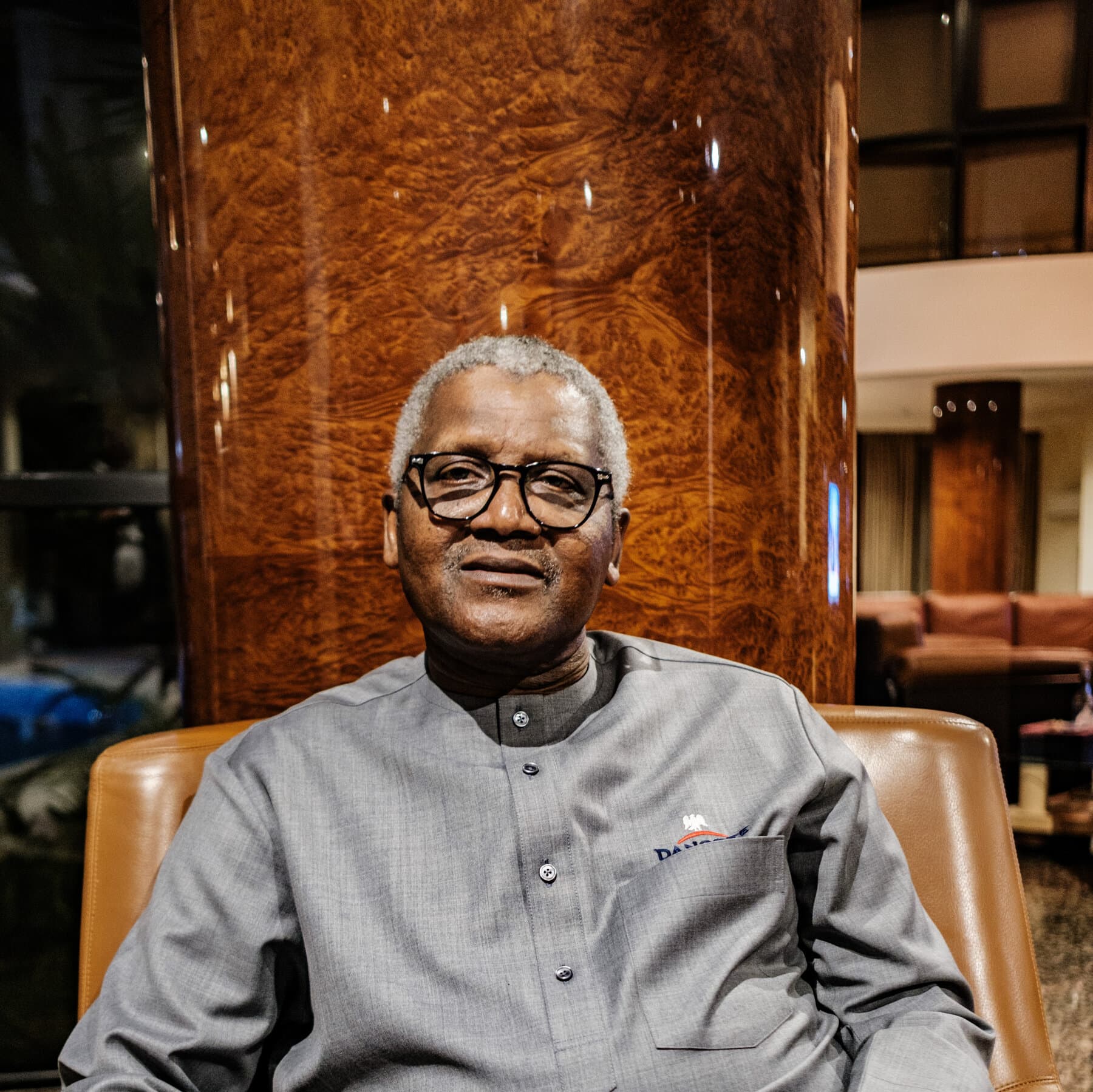 A hyper-realistic, high-contrast image showing a gleaming, futuristic oil refinery in the background, contrasting sharply with a rusted, broken pipeline in the foreground. In the distance, a chaotic line of cars waits for fuel under a hazy, smog-filled sky.