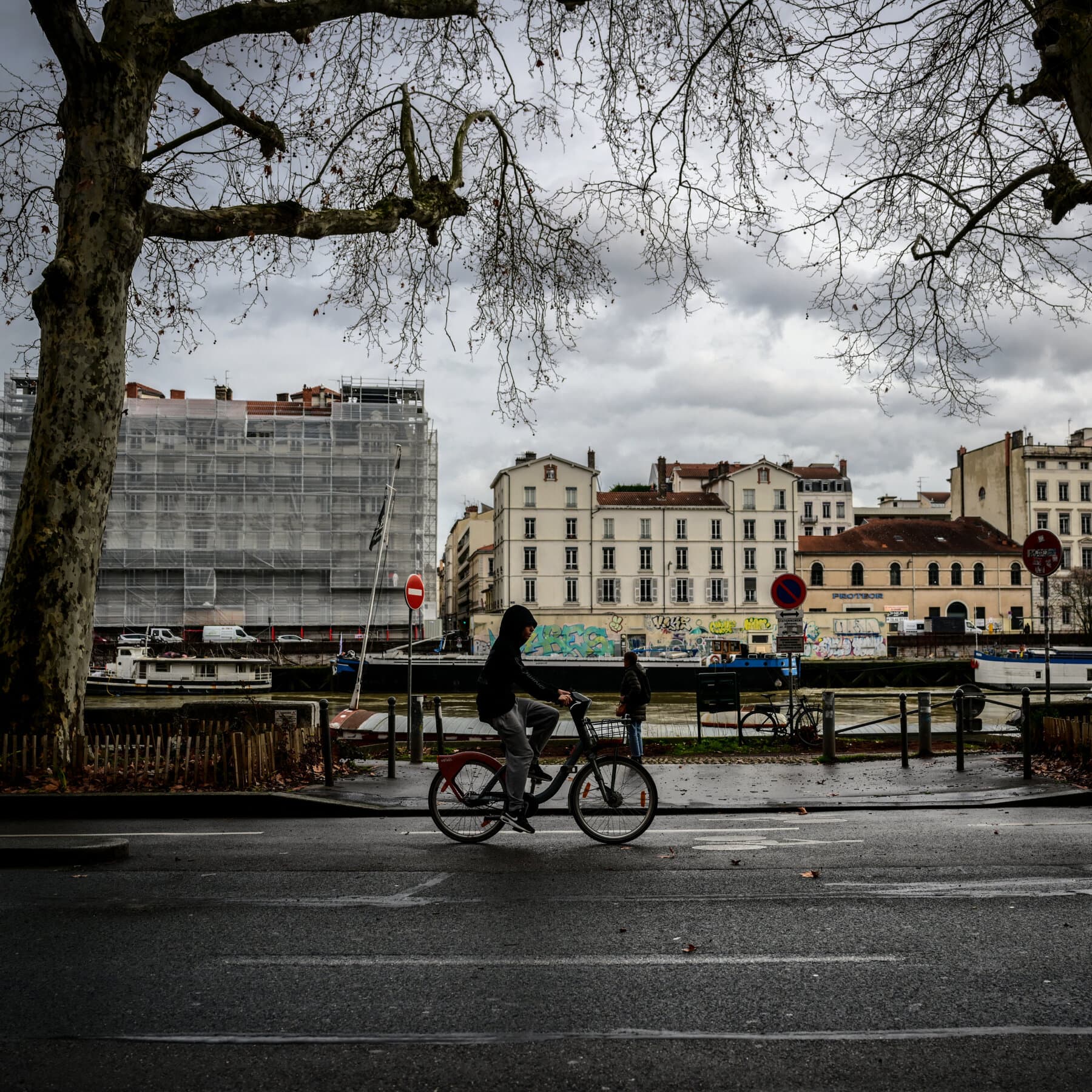 A gritty, abstract illustration in a dark, cynical style. A silhouette of a fallen figure lies on the ground in grayscale. Above the figure, two large, distorted hands—one red, one blue—are reaching down, not to help, but to grab. The background is a blurry, chaotic French street scene with muted colors. The atmosphere is gloomy, tense, and oppressive.