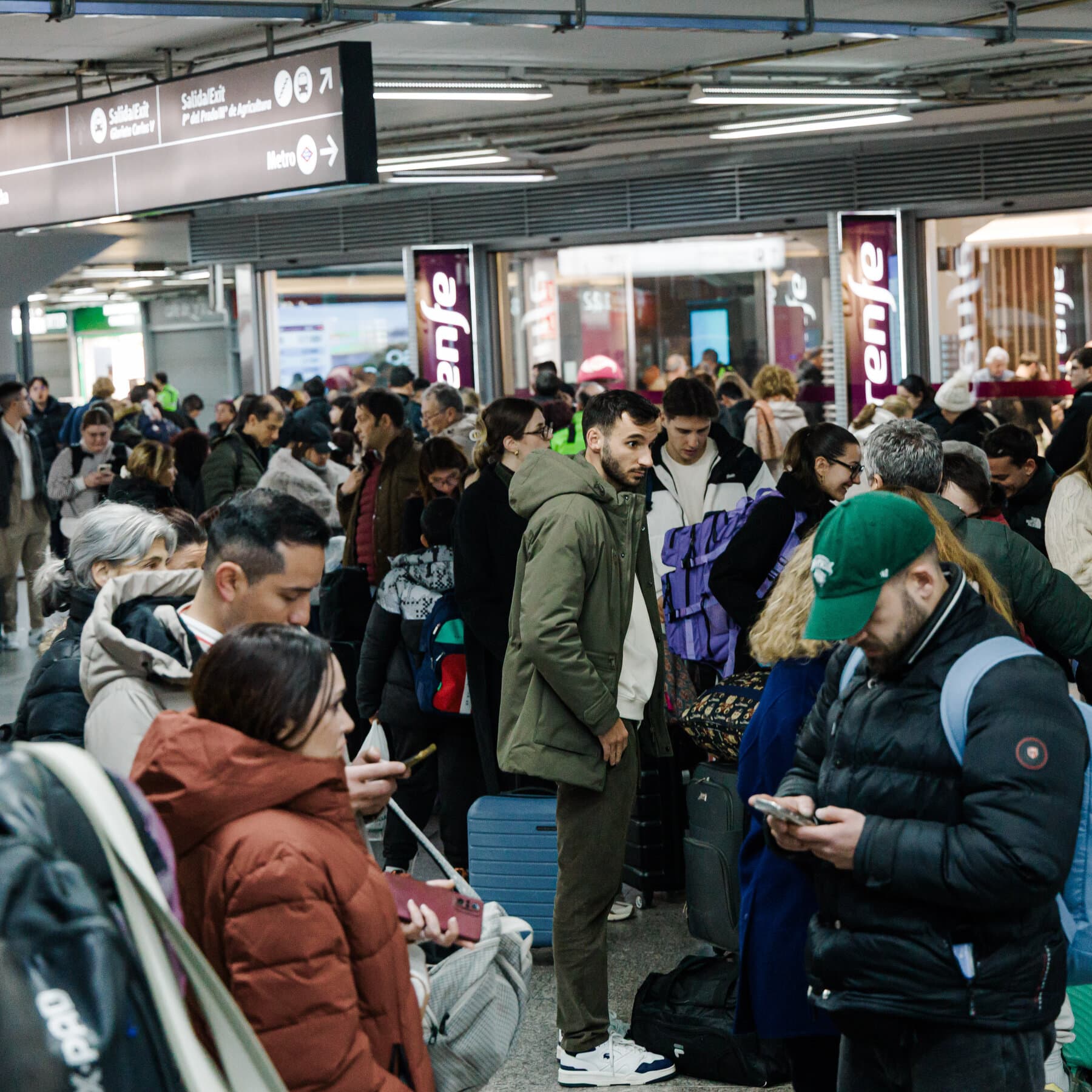 A wide, cinematic shot of two crumpled, white high-speed trains on a desolate Spanish rail track under a harsh, glaring sun. Smoke rises from the wreckage, and the surrounding landscape is dry and yellowed. In the foreground, a single, pristine rail signal light is turned off. The style is hyper-realistic with a cold, cynical color palette.