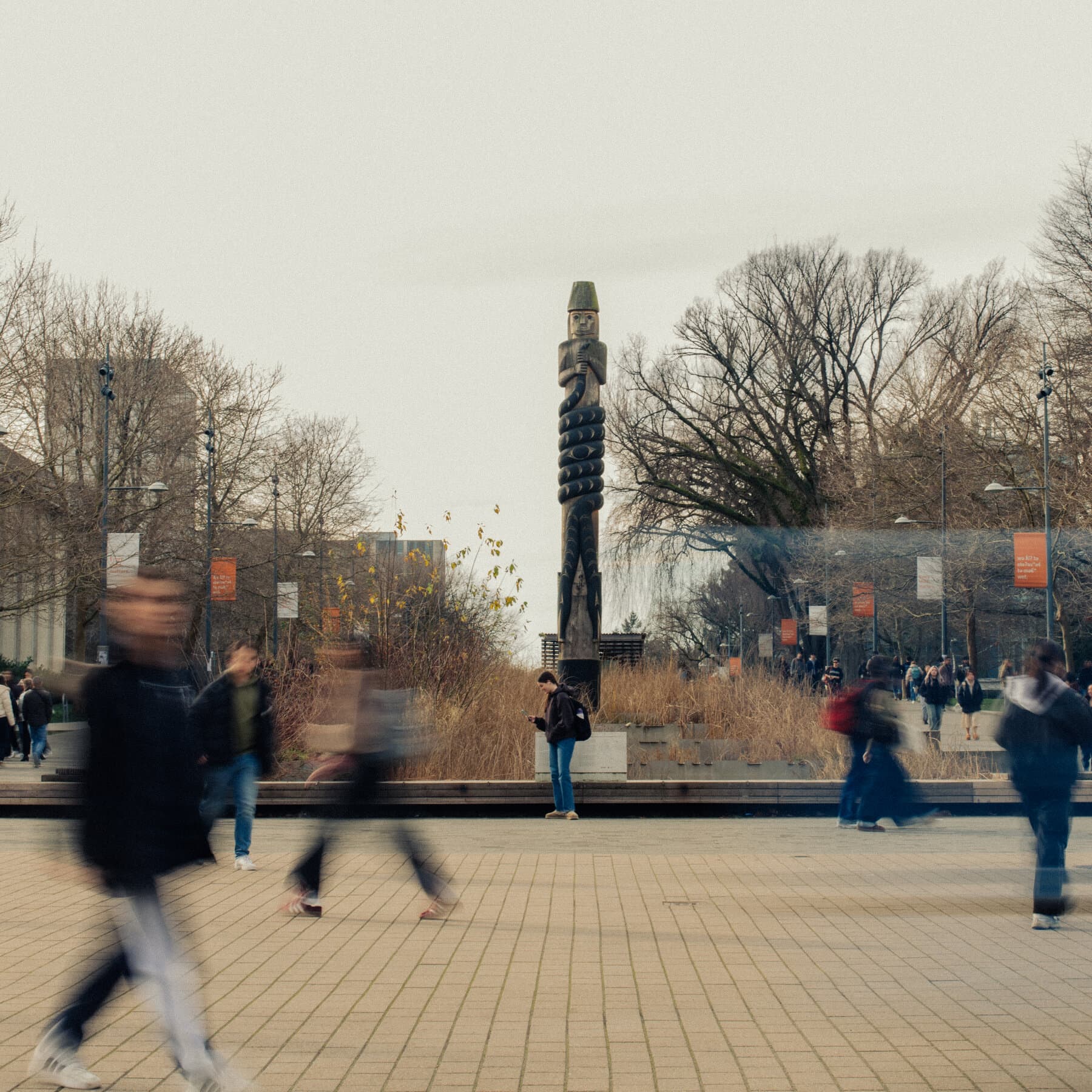 A hyper-realistic, satirical editorial illustration showing a crumbling ivory tower made of old books. At the base, men and women in academic robes are fighting over a piece of paper while a judge looks on with boredom. The background is a grey, rainy Vancouver sky.