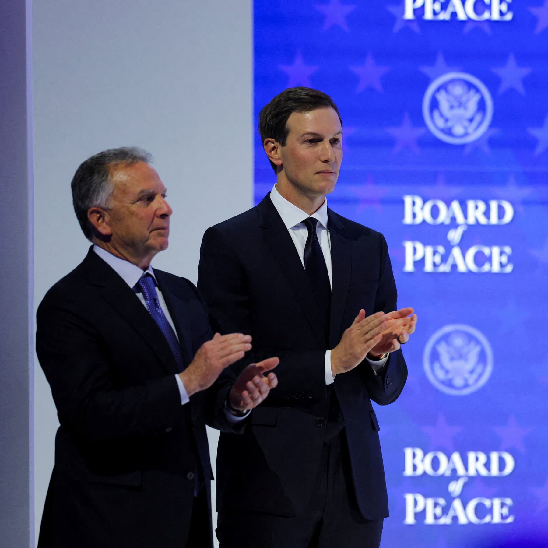 A surreal, gritty oil painting style image. In the center, a polished mahogany boardroom table sits amidst a smoking, rubble-filled battlefield. Two empty, expensive business suits float above the chairs as if invisible men are wearing them. On the table, a map of the world is being cut up with a golden knife and fork. Dark, muted colors with flashes of neon red. High contrast.