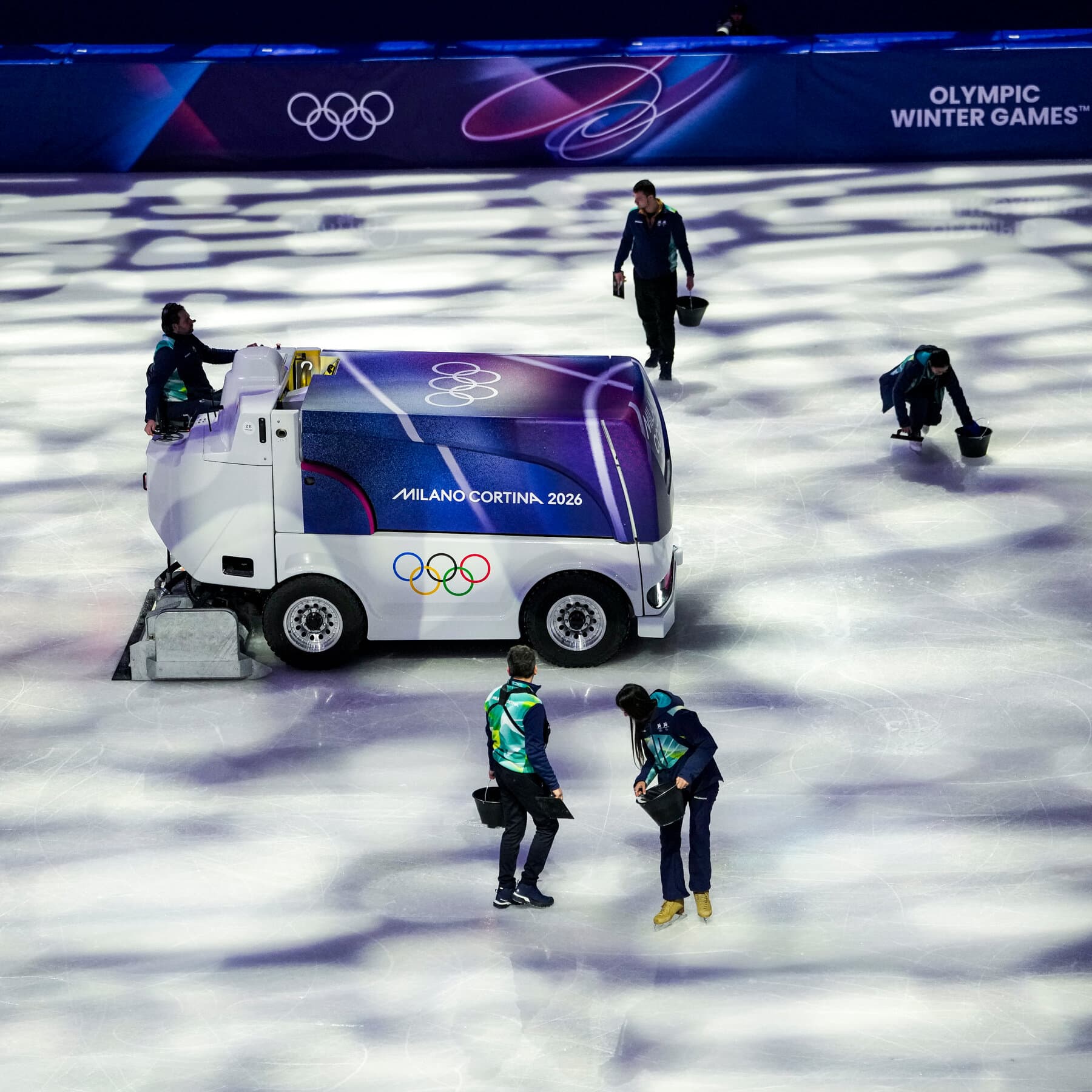 A moody, high-contrast image inside an Olympic arena. A single Zamboni ice resurfacer is driving on the ice, casting a long shadow. In the foreground, an ice technician in a heavy winter coat is kneeling on the ice, examining it with a magnifying glass and a digital thermometer, looking extremely serious. The stadium seats are empty and dark, putting all the focus on the absurdly clinical inspection of the frozen floor. Cold blue lighting.
