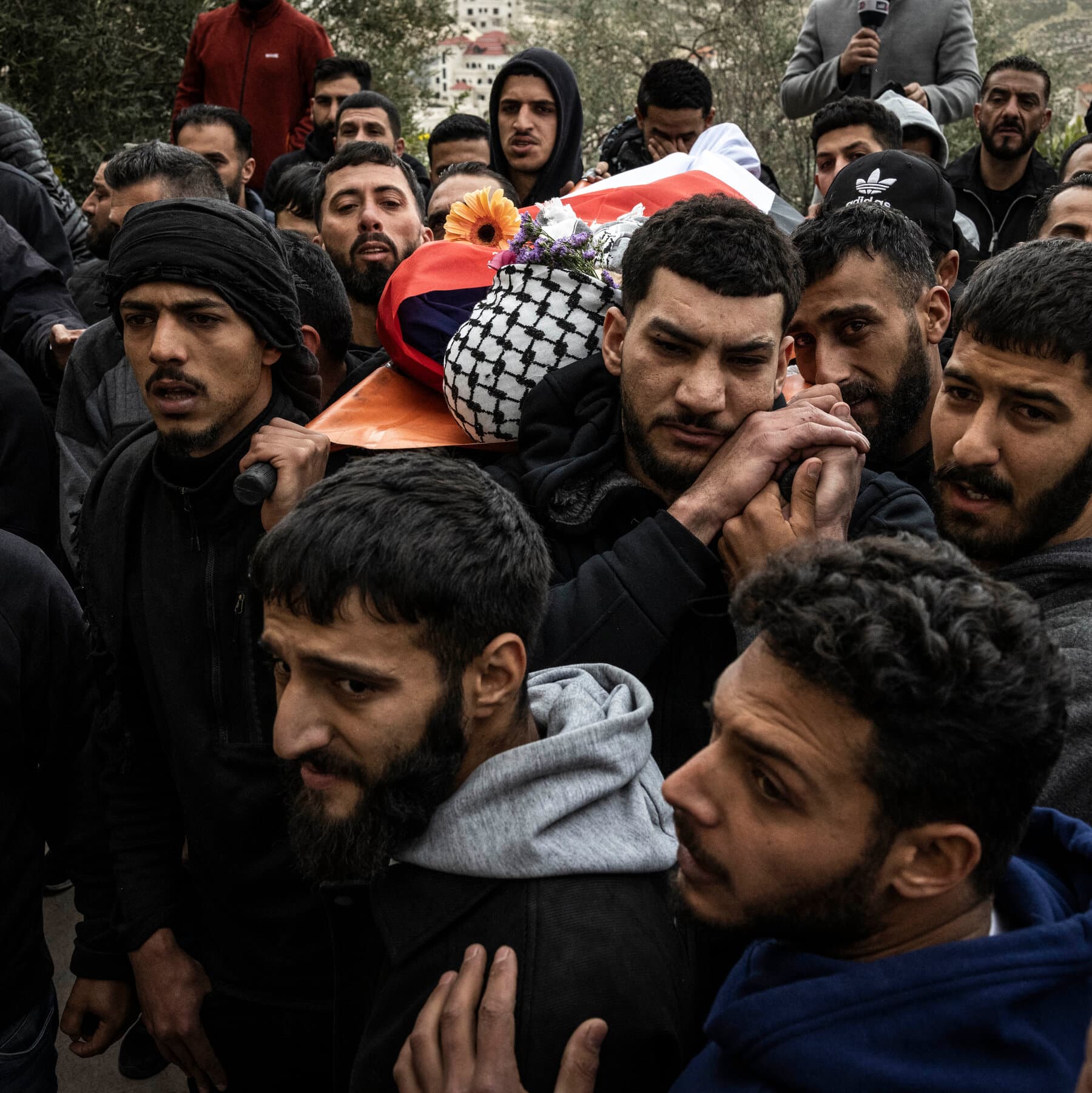 A gritty, high-contrast black and white photo of a dusty, rocky ground in the West Bank. In the center, half-buried in the dirt, is a generic blue passport, closed and worn. In the background, out of focus, a barbed wire fence stretches across the horizon under a harsh, bright sun. No people, just the desolate landscape and the discarded document.