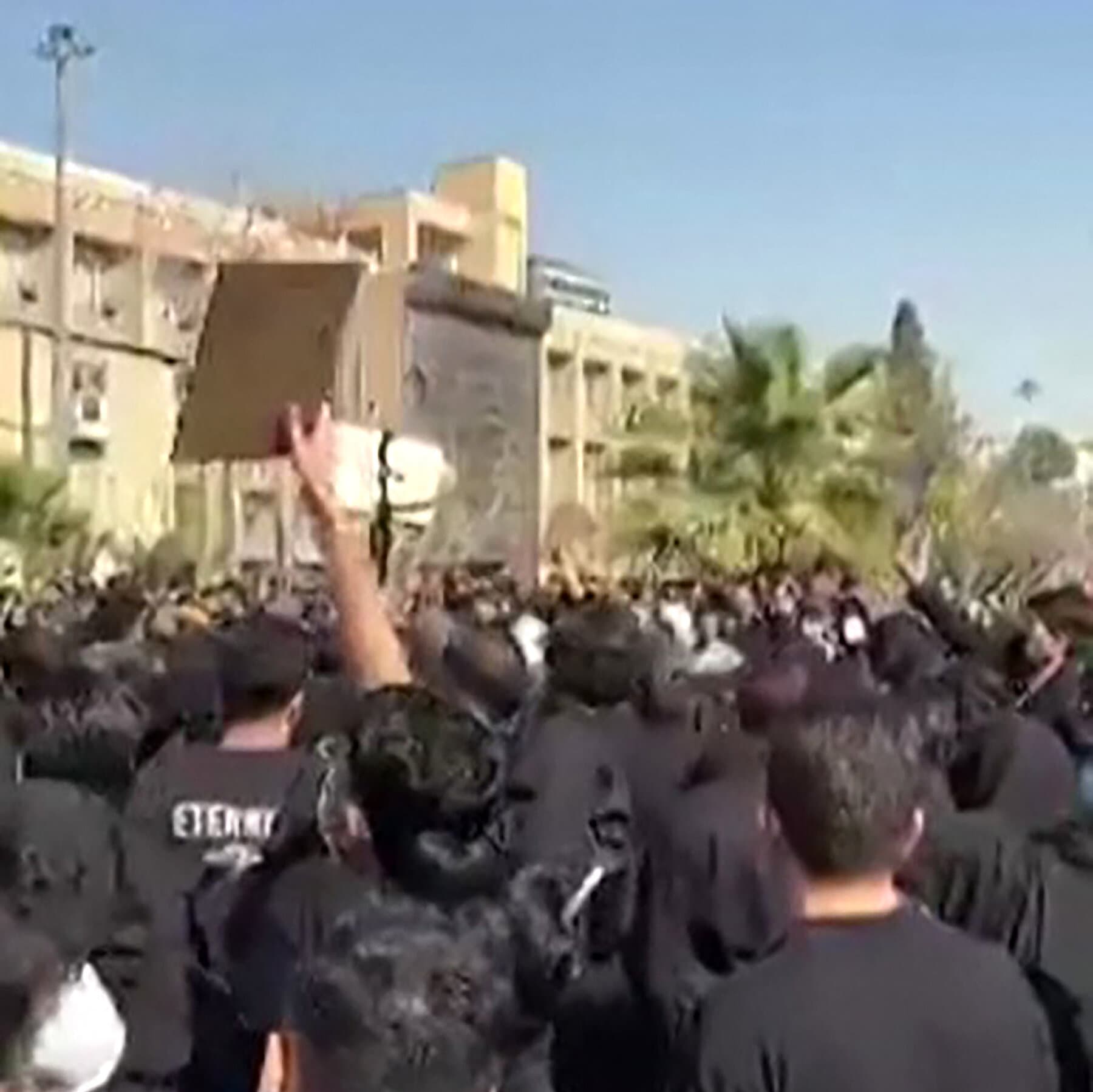 A gritty, high-contrast illustration in a noir graphic novel style. A large iron university gate stands open. On one side, a sea of young people in silhouette are shouting, their forms sharp and energetic. On the other side, towering over them, are large, crumbling stone statues of old men in suits, cracking and gray. The sky is a heavy, oppressive charcoal color, but the students are highlighted with faint, defiant red outlines. The atmosphere is tense and gloomy.