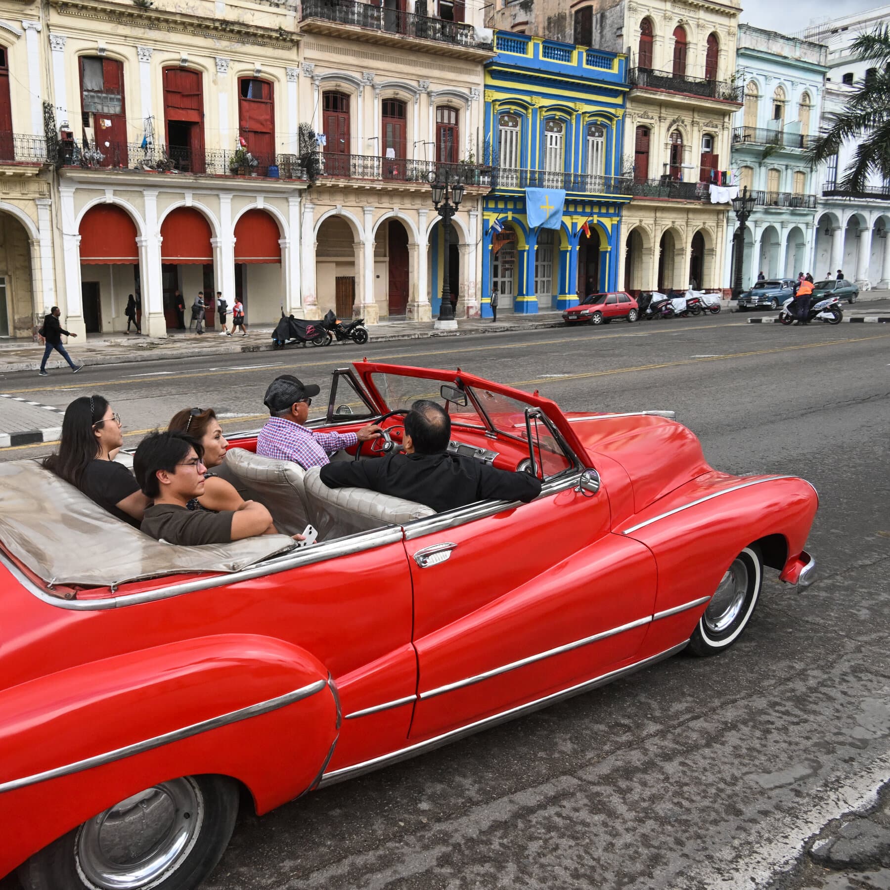 A desolate street in Havana at twilight with a stalled, dusty 1950s American car in the foreground. In the background, a grand but decaying hotel with dark windows, no lights on. The sky is a bruised purple. The atmosphere is lonely and silent.