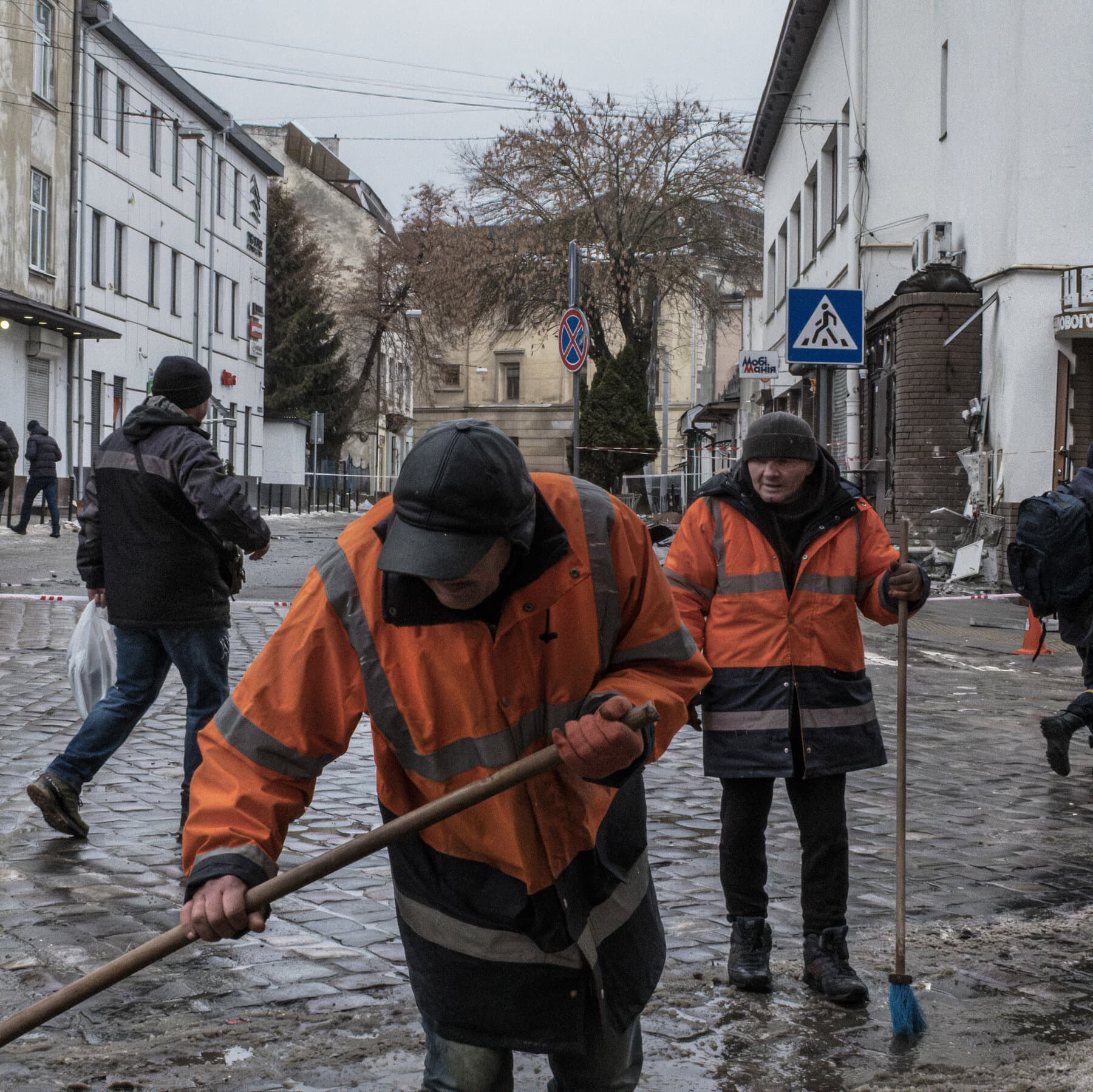 A gritty, cynical editorial illustration in greyscale. A crumbling concrete birthday cake sits on a ruined table in the middle of a debris field. Instead of candles, four smoking missiles are stuck into the top of the cake. In the background, a dark, smoky skyline of Kyiv under a grey sky. The style should be sketched and rough, emphasizing despair and irony.