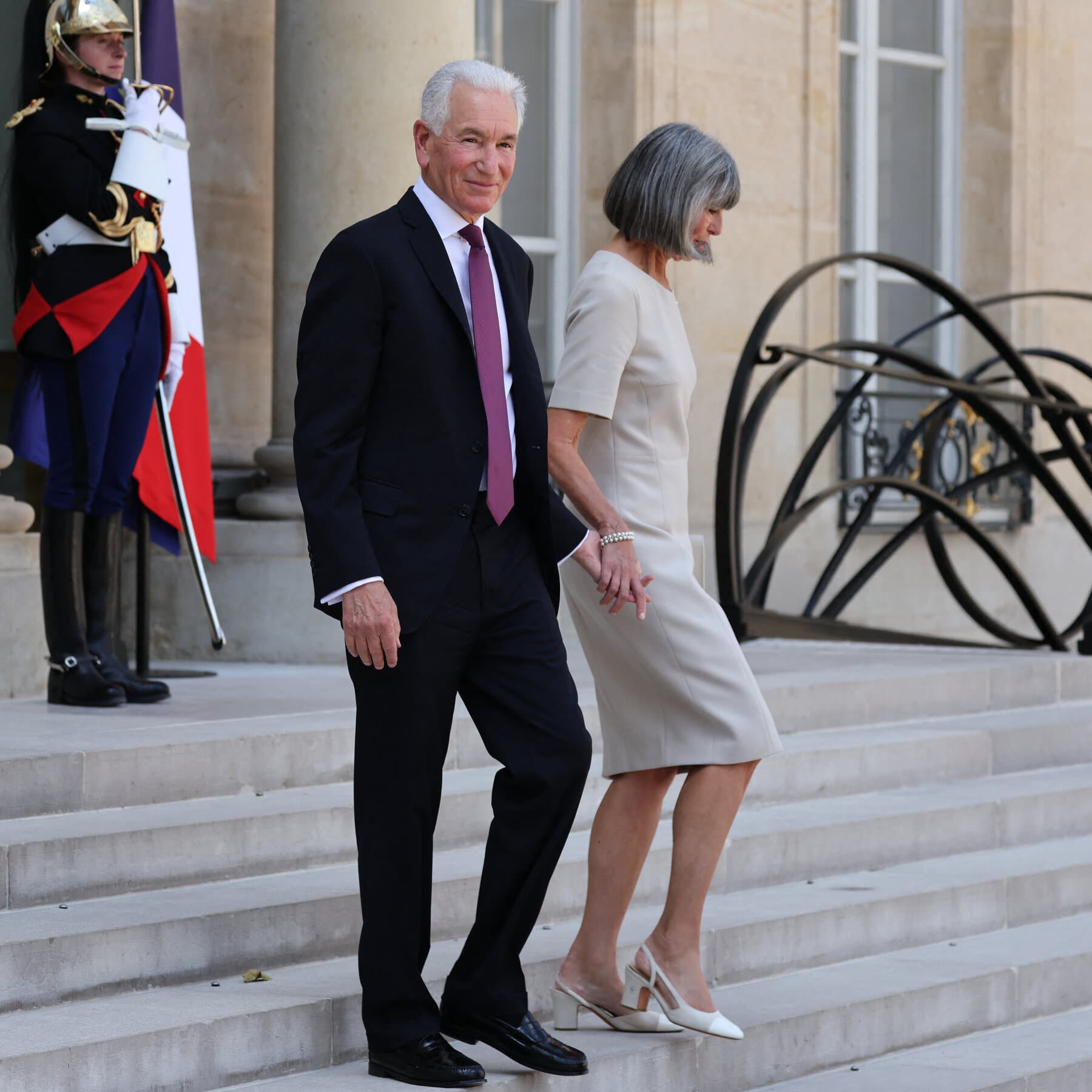 A conceptual illustration in a satirical editorial style. In the foreground, a classic, ornate French diplomatic room with velvet curtains. On one side, a shadowy, sleek figure representing the U.S. wearing a suit, holding a jagged mirror that distorts the reflection of the room. In the reflection, the peaceful room looks like a chaotic fire. On the other side, a weary French diplomat in a sash looks on with exhaustion. The atmosphere is cynical, moody, and slightly surreal. Muted colors of blue, red, and grey.