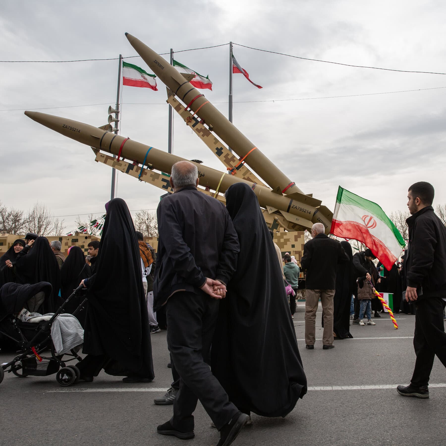 A gritty, high-contrast political cartoon style illustration. A poker table in a dark, smoky room. On one side, a figure representing Iranian leadership holds a hand of cards that are actually lit sticks of dynamite. On the other side, a figure representing Uncle Sam points a stern finger. The atmosphere is tense and noir-inspired. No text.