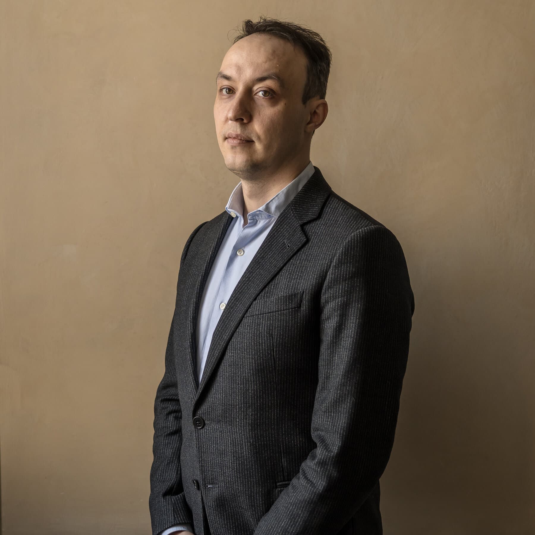 A hyper-realistic, desaturated editorial illustration of a weary man in a gray business suit standing in an endless corridor filled with floating red tape and stacks of paper. He is looking at a calendar on the wall where the year 2026 is glowing faintly. In the background, vague silhouettes of politicians are drinking coffee, ignoring him. The mood is cynical, cold, and bureaucratic.