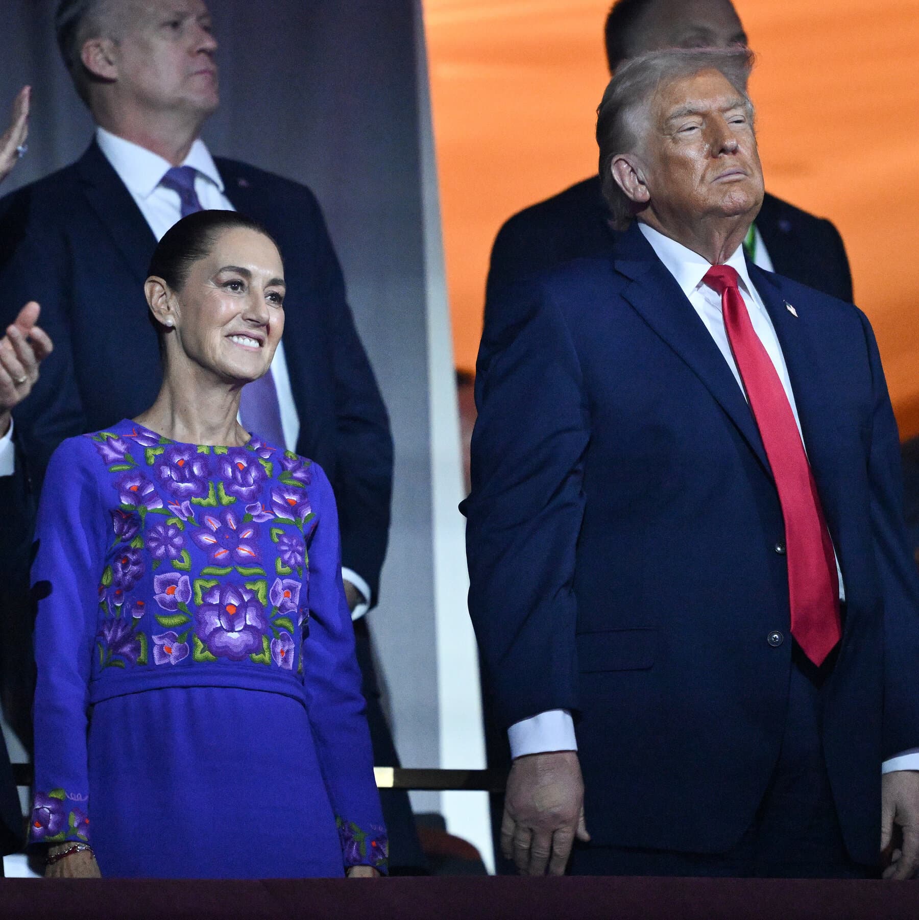 A gritty, high-contrast noir illustration of a dusty Mexican street. In the foreground, a crumpled newspaper on the asphalt shows a blurred photo of a crime boss. In the background, two massive, looming shadows cast over the town: one shadow is shaped like a man in a suit shouting, the other shadow is a group of figures holding rifles. The lighting is dim and oppressive.