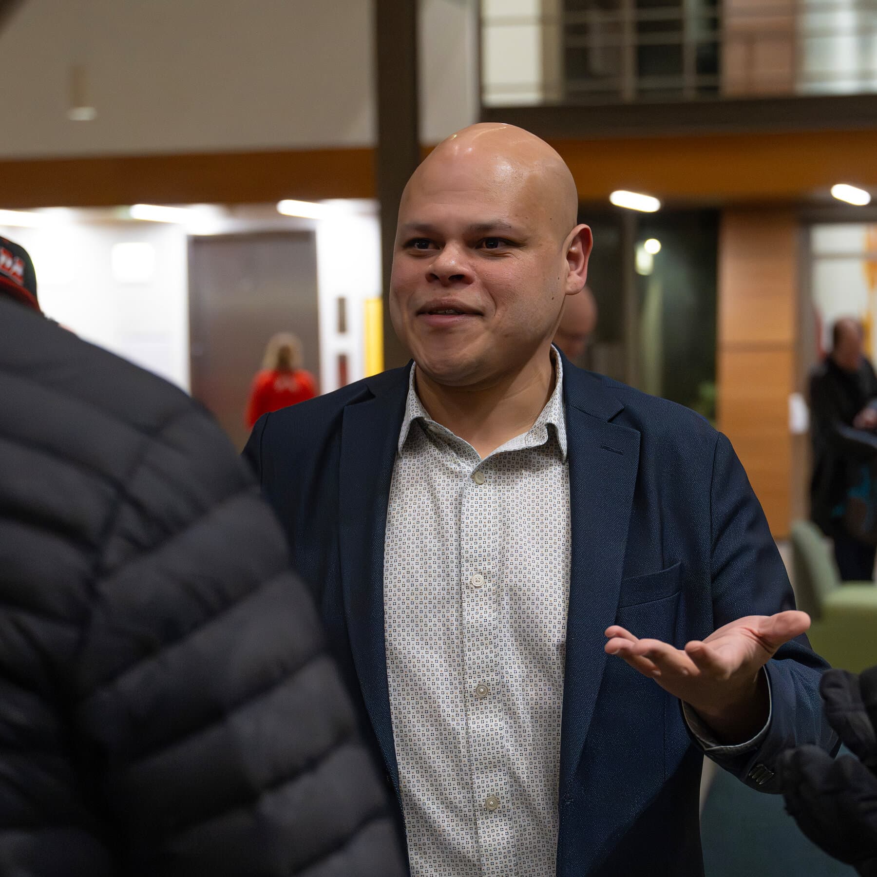 A satirical illustration of a Canadian beaver wearing a red baseball cap and holding a megaphone, standing on a soapbox in front of a university building. The beaver looks angry and is shouting. In the background, a maple leaf flag is slowly transforming into the stars and stripes. The style is gritty, cynical political cartoon, muted colors with splashes of red.