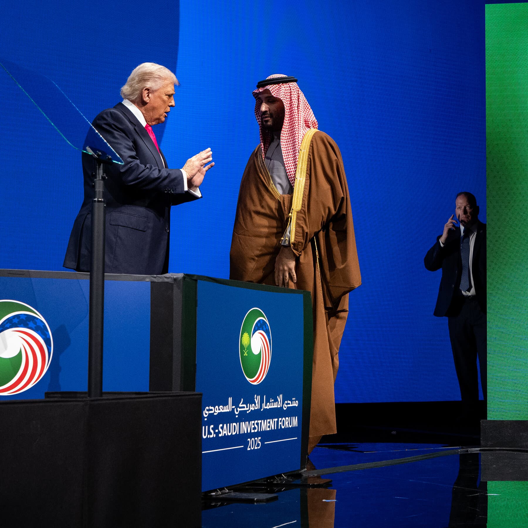 A satirical, surreal oil painting style illustration. Two golden, ornate thrones sit on a cracked desert floor, facing away from each other. Between them is a tangled mess of old-fashioned telephone wires connecting to a large, looming, shadowy figure of a man in a suit in the background. In the distance, smoke rises from a map of Sudan. The lighting is dramatic and moody, emphasizing the separation and the chaos.