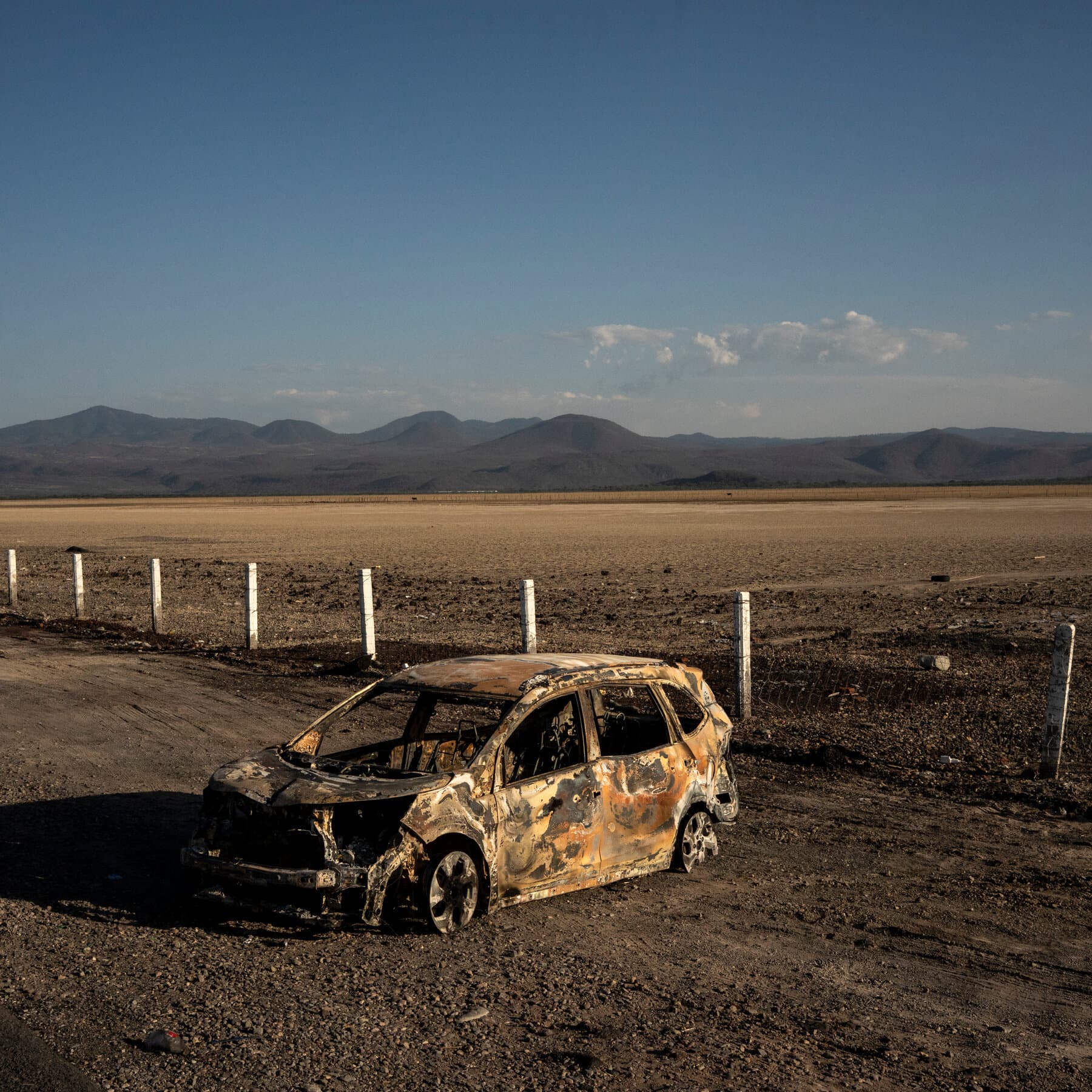 A gritty, black and white political cartoon style illustration showing a large, empty, crumbling stone throne sitting in the middle of a vast desert. On the seat of the throne is a generic suit jacket, empty, with no person inside. In the background, a storm of money and skulls swirls in the wind. The atmosphere is dusty and bleak.