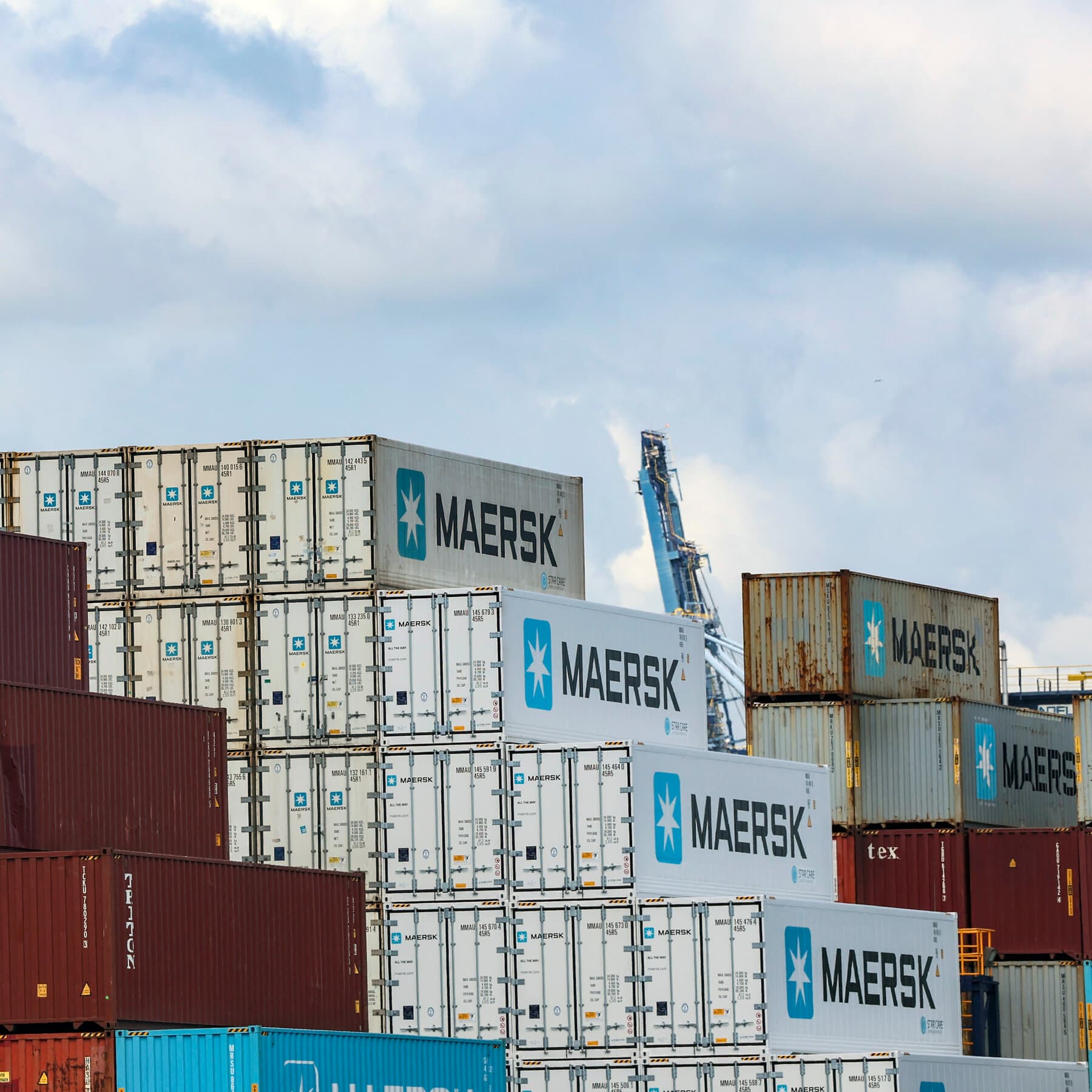 A massive, rusty container ship turning around in rough, dark ocean waters. In the background, a dusty, desolate coastline with smoke rising from it. The sky is grey and stormy. High contrast, gritty, realistic style.
