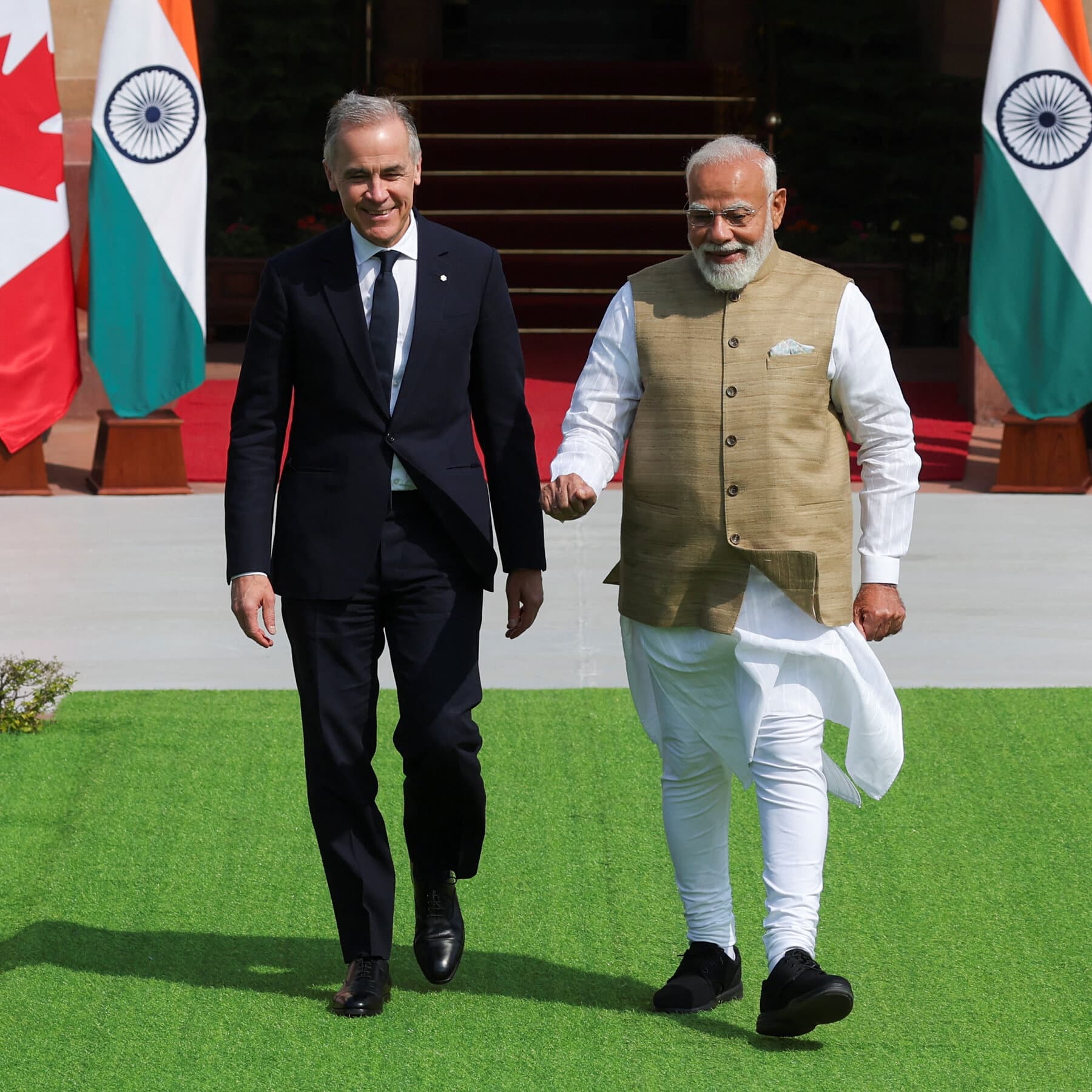 A hyper-realistic, gritty satirical illustration showing two men in expensive dark suits shaking hands over a conference table. The table is actually a dirty rug. Under the rug, the distinct shape of a human body is visible, creating a lump in the rug. The man on the left represents a Canadian leader, looking tired and desperate. The man on the right represents the Indian leader, looking smug and powerful. On the table, instead of water bottles, there are stacks of cash and a spilled glass of red wine that looks like blood. The lighting is dim, harsh, and cynical, like a noir detective movie.
