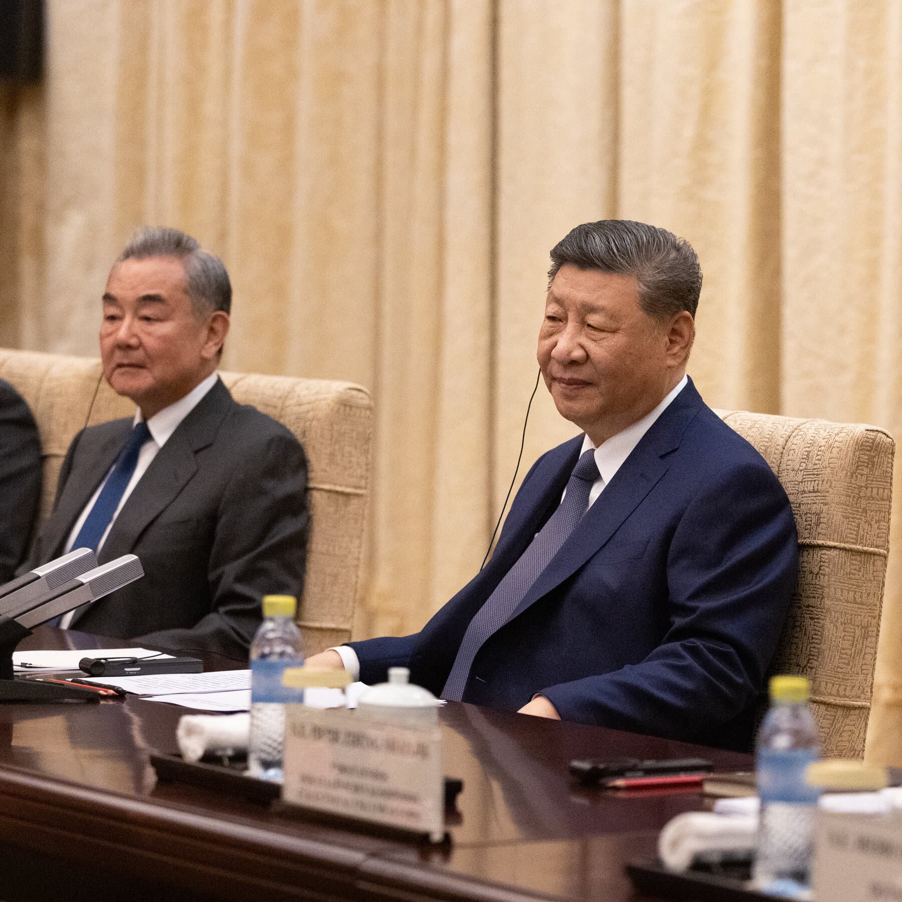 A gritty, high-contrast illustration of a poker table where two faceless men in suits are shaking hands over a pile of money, while a small toy soldier burns in the ashtray between them. Muted colors, dark atmosphere.
