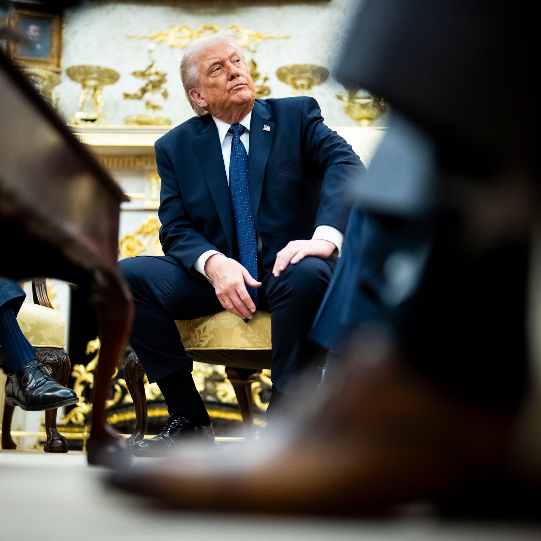 A minimalist, satirical illustration showing a large, angry red tie tying itself into a knot around a bottle of olive oil and a leg of ham, set against a plain beige background. The style should be like a political cartoon, simple and flat.