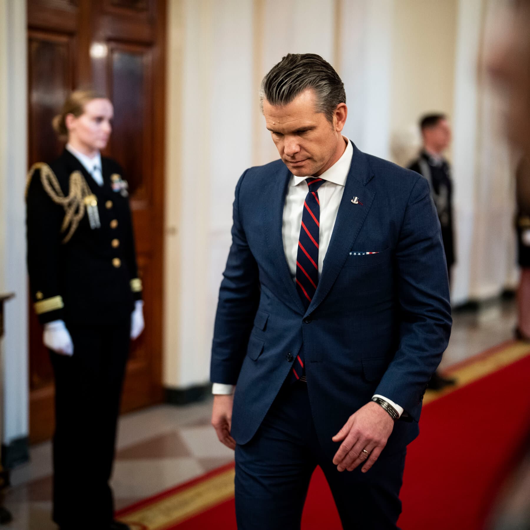 A hyper-realistic, gritty satirical image of a politician wearing a flight suit and aviator sunglasses, giving a thumbs up and smiling widely. He is standing in front of a somber military graveyard with fresh dirt mounds. The scene is lit with harsh, stage-style spotlights, contrasting the fake celebration with the grim reality. The style should be cynical and high-contrast.