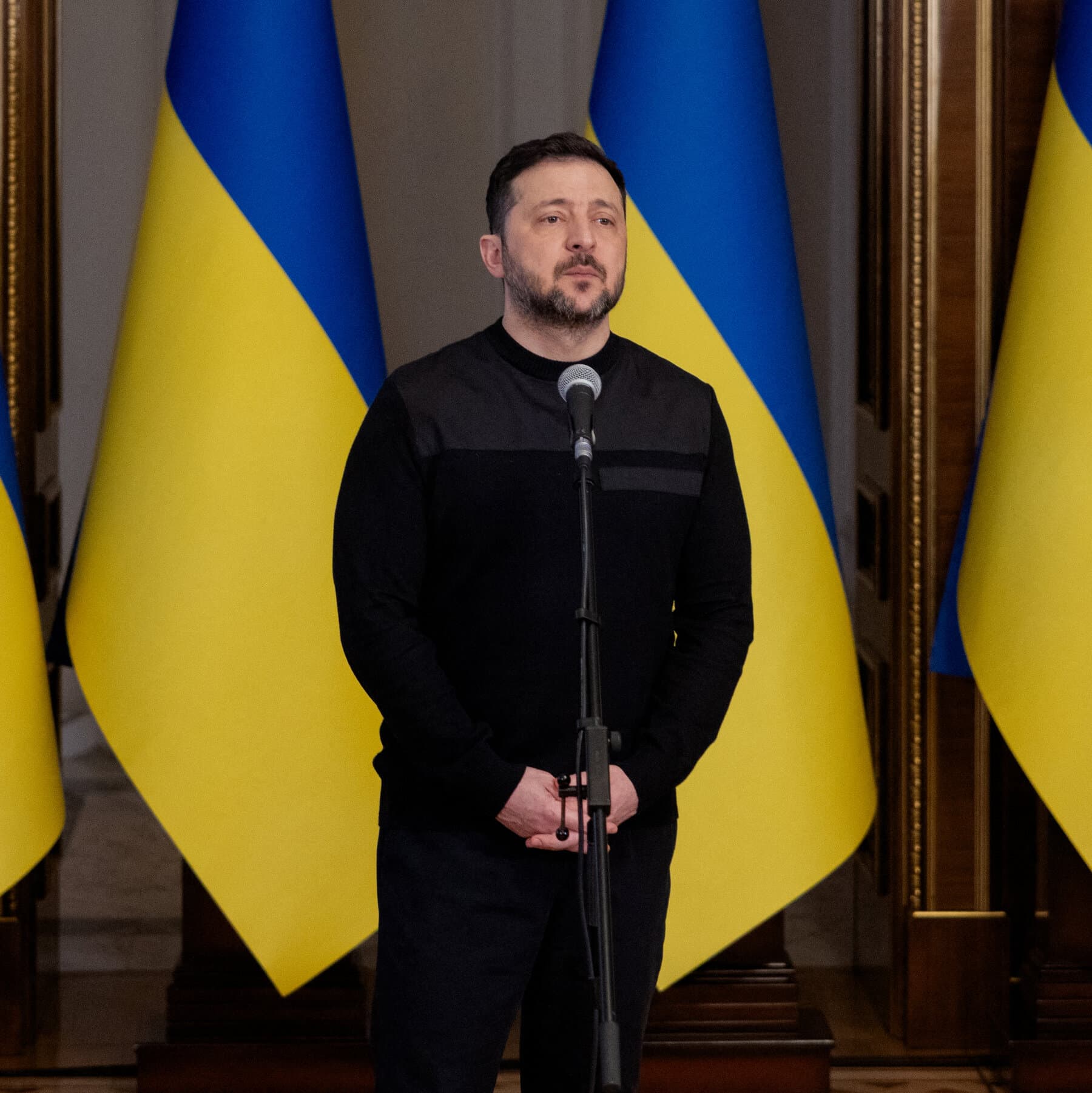 A cynical political cartoon style illustration showing a large, distracted Uncle Sam figure turning his back on a freezing, battered soldier in a trench labeled 'Ukraine' to look at a fiery explosion in a desert labeled 'Mideast', while holding a single, small shield that cannot cover both.